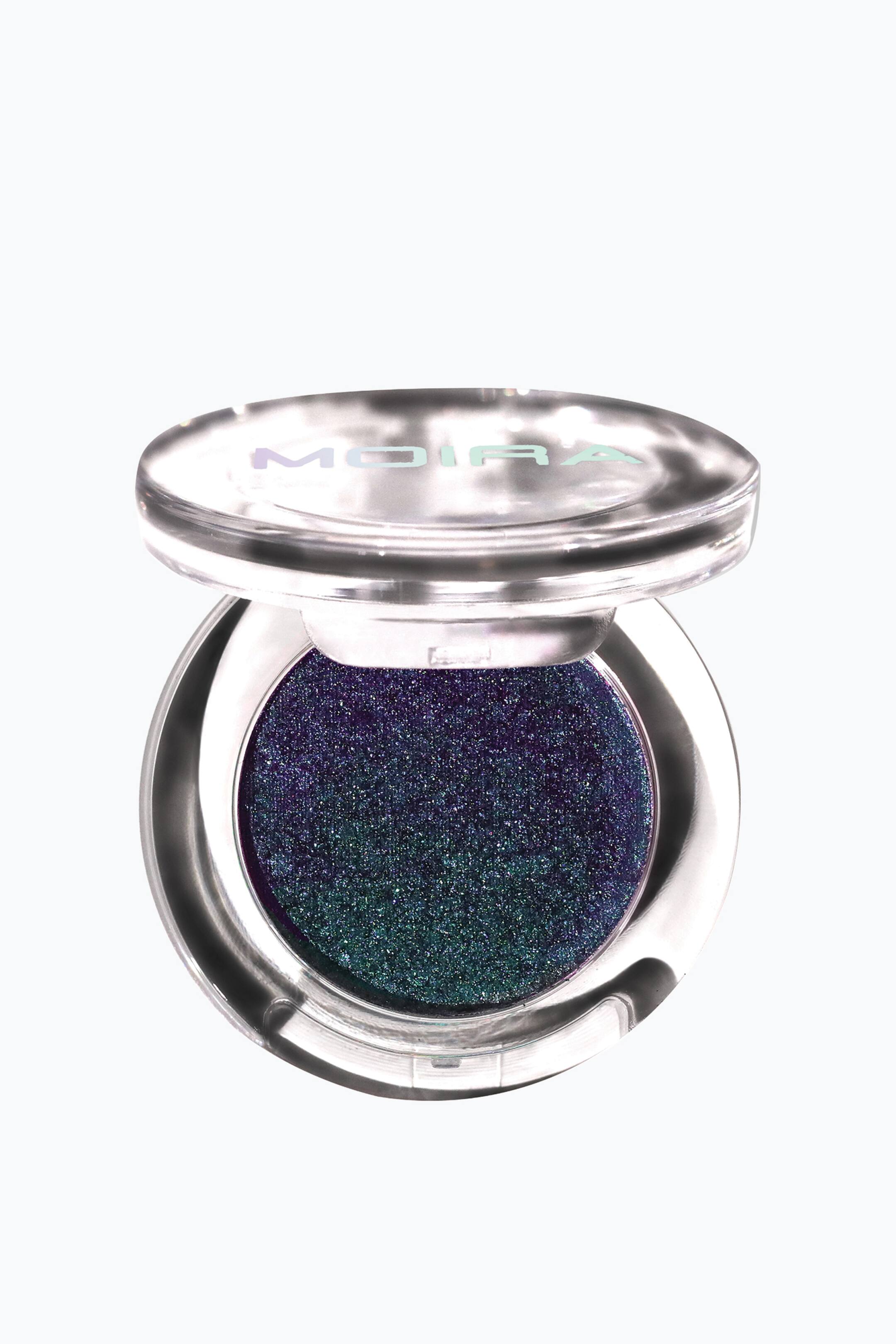 Vis større bilde: Supernova Glitz Shadow vises i et åpent, rundt, transparent akrylkompakt med en sølvfarget innerkant, og fremhever én panne med teksturert, dyp lilla og teal duokrom glitter. Det gjennomsiktige lokket står åpent på toppen og avslører merkenavnet «MOIRA» trykt i holografisk skrift.