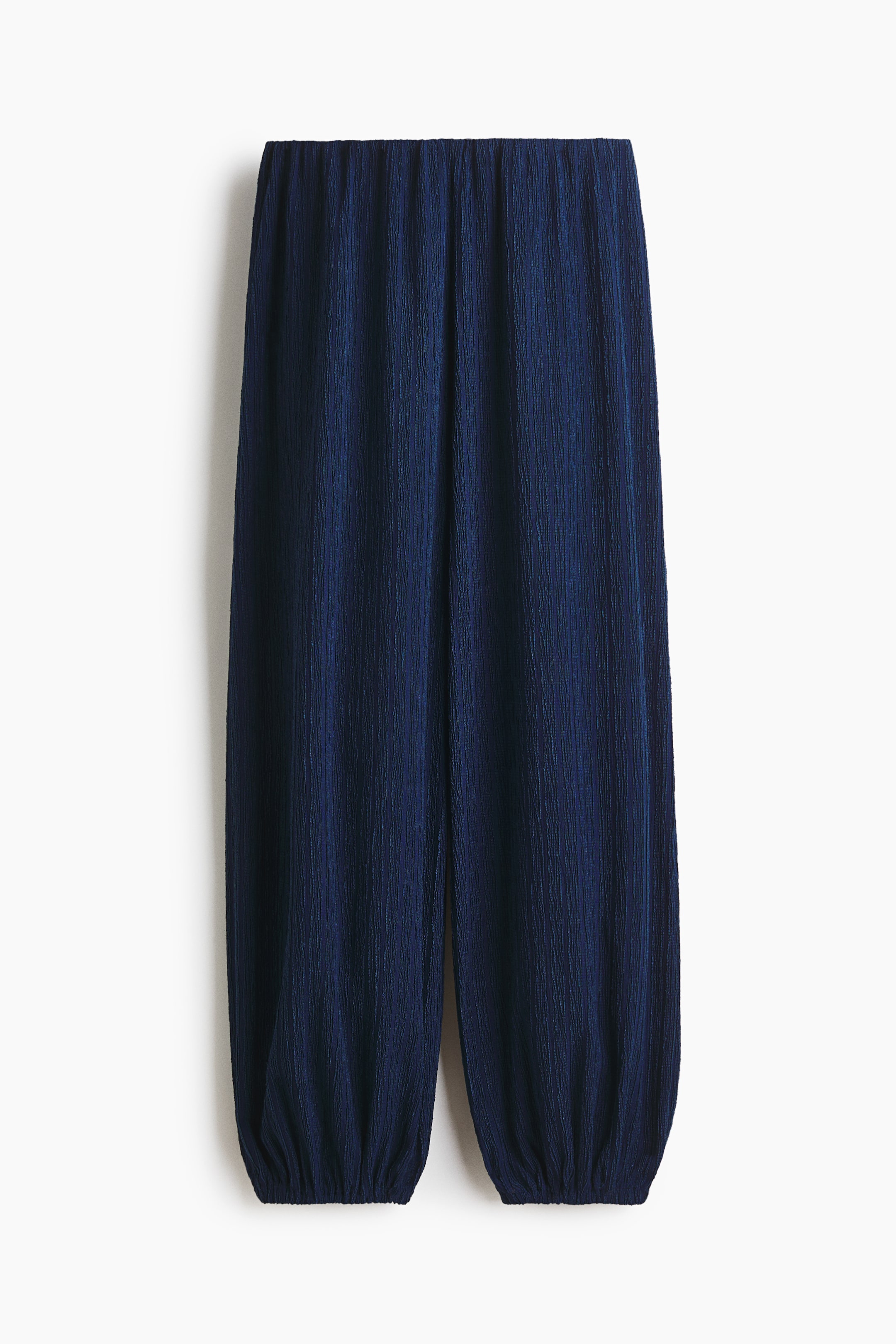View larger image: Navy blue pants feature an elasticated waistband and a crinkled, vertically textured fabric. The loose-fitting legs gather at the elasticated cuffs.