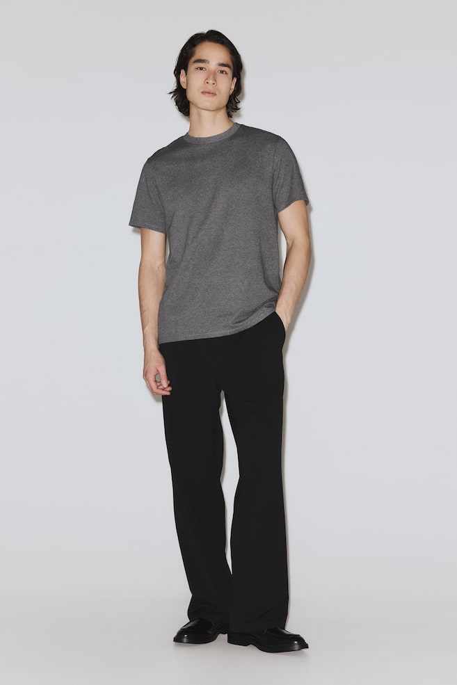 A dark grey crewneck T-shirt is being worn, featuring short sleeves and a straight hem. It displays a subtle heathered texture and a classic fit. - 1