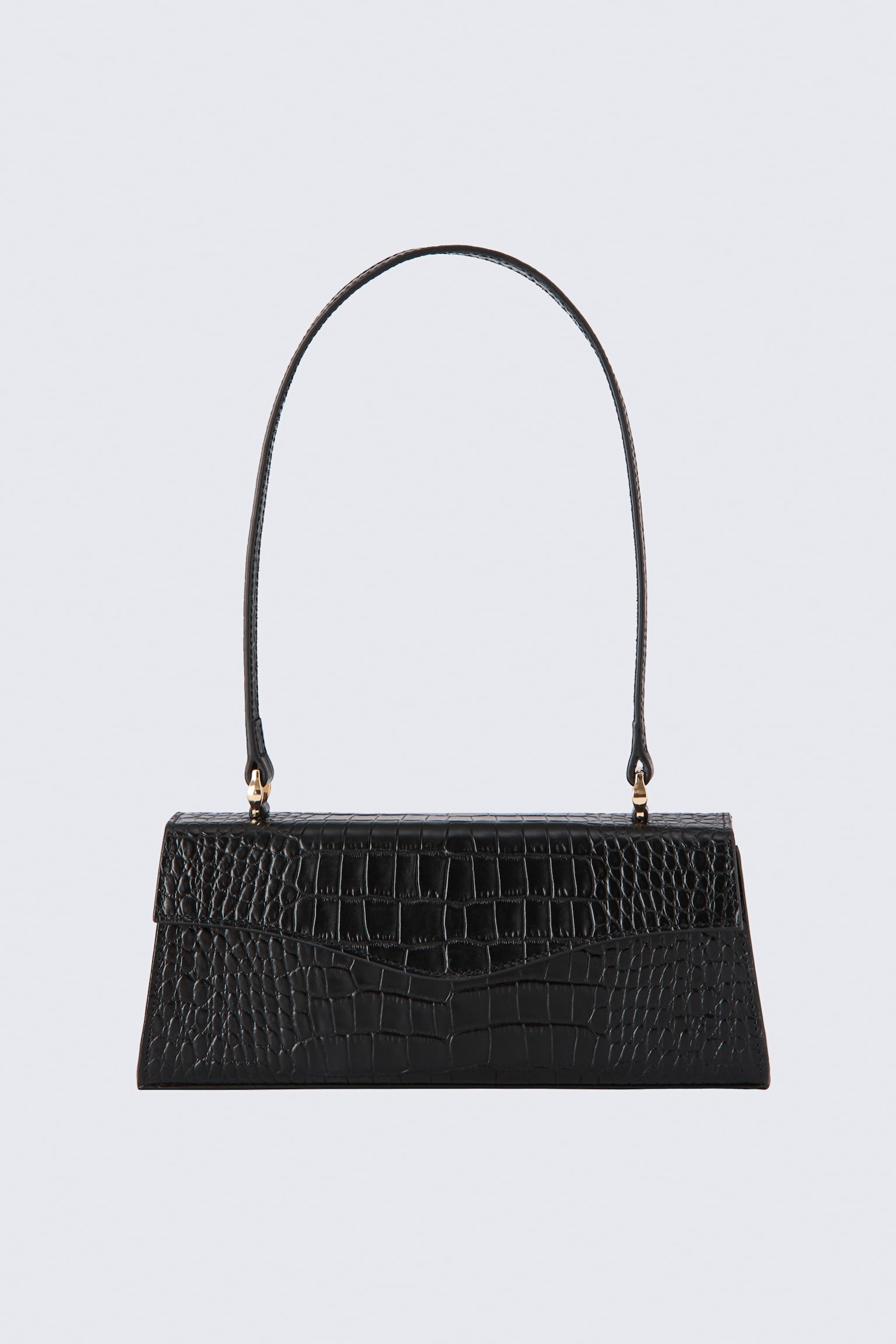 Un bolso de hombro de cuero negro estÃ¡ orientado hacia el frente, mostrando una forma estructurada trapezoidal con textura grabada tipo cocodrilo. El bolso presenta una solapa frontal curvada y una larga y delgada correa de hombro arqueada, sujeta con herrajes en tono dorado.
