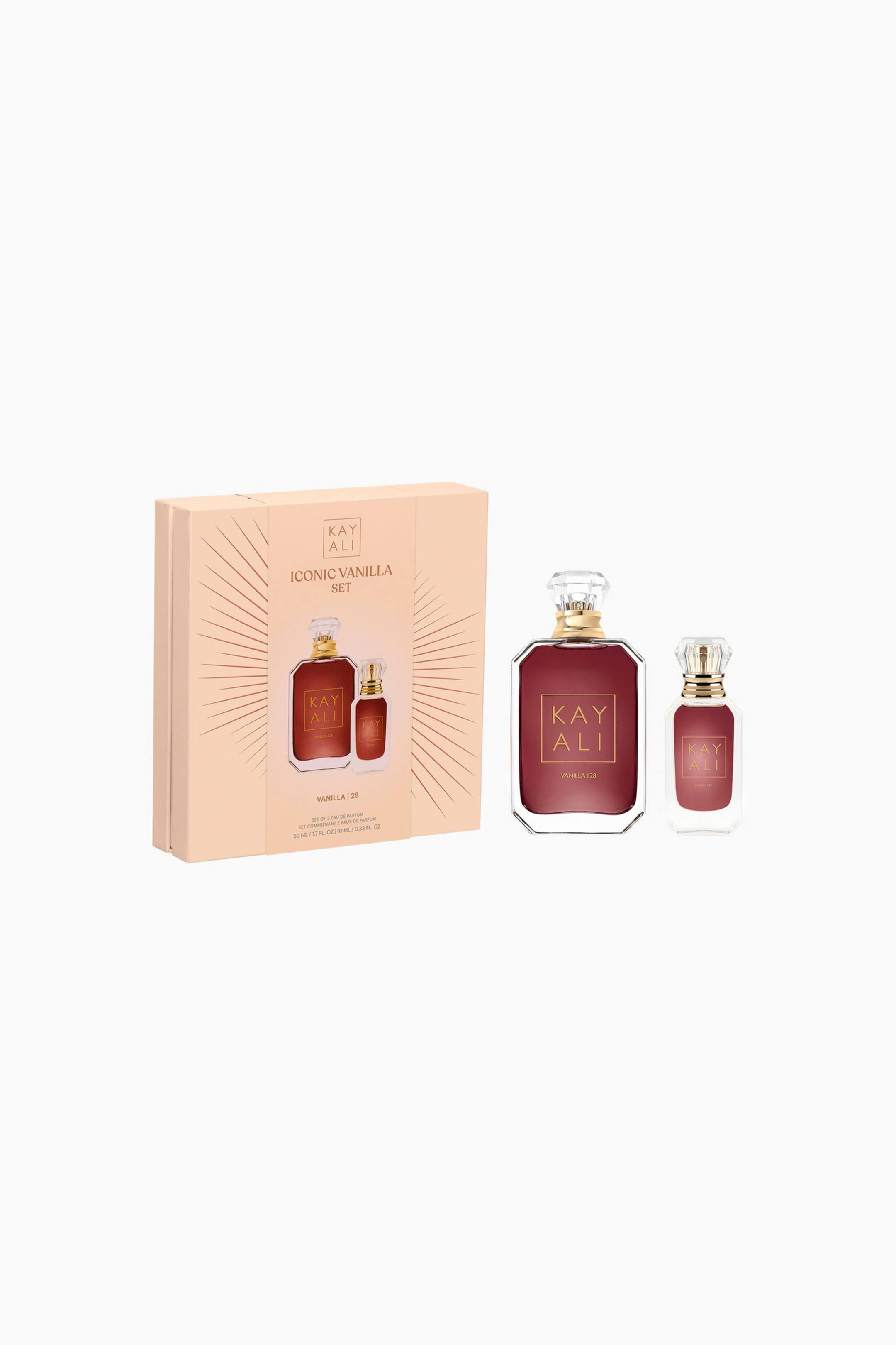 Vis større bilde: Et Kay Ali Iconic Vanilla Set viser frem en lys ferskenfarget eske, vinklet litt til høyre, med bilder av to parfymeflasker på forsiden. En større rektangulær parfymeflaske og en mindre matchende flaske står oppreist til høyre, begge med mørkerød væske, gullfargede halser og klare, fasetterte korker.