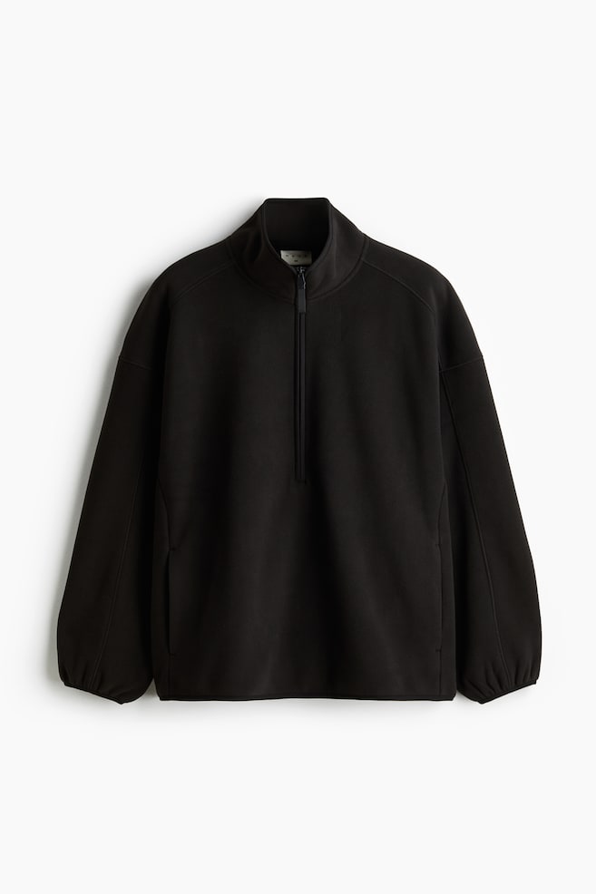 Un jersey de forro polar negro de ajuste holgado aparece de frente, con un cuello alto que enmarca su cuello y un cierre de media cremallera negro que se extiende por su pecho. Sus mangas largas terminan en puños recogidos, y costuras prominentes definen los hombros y los lados. - 1