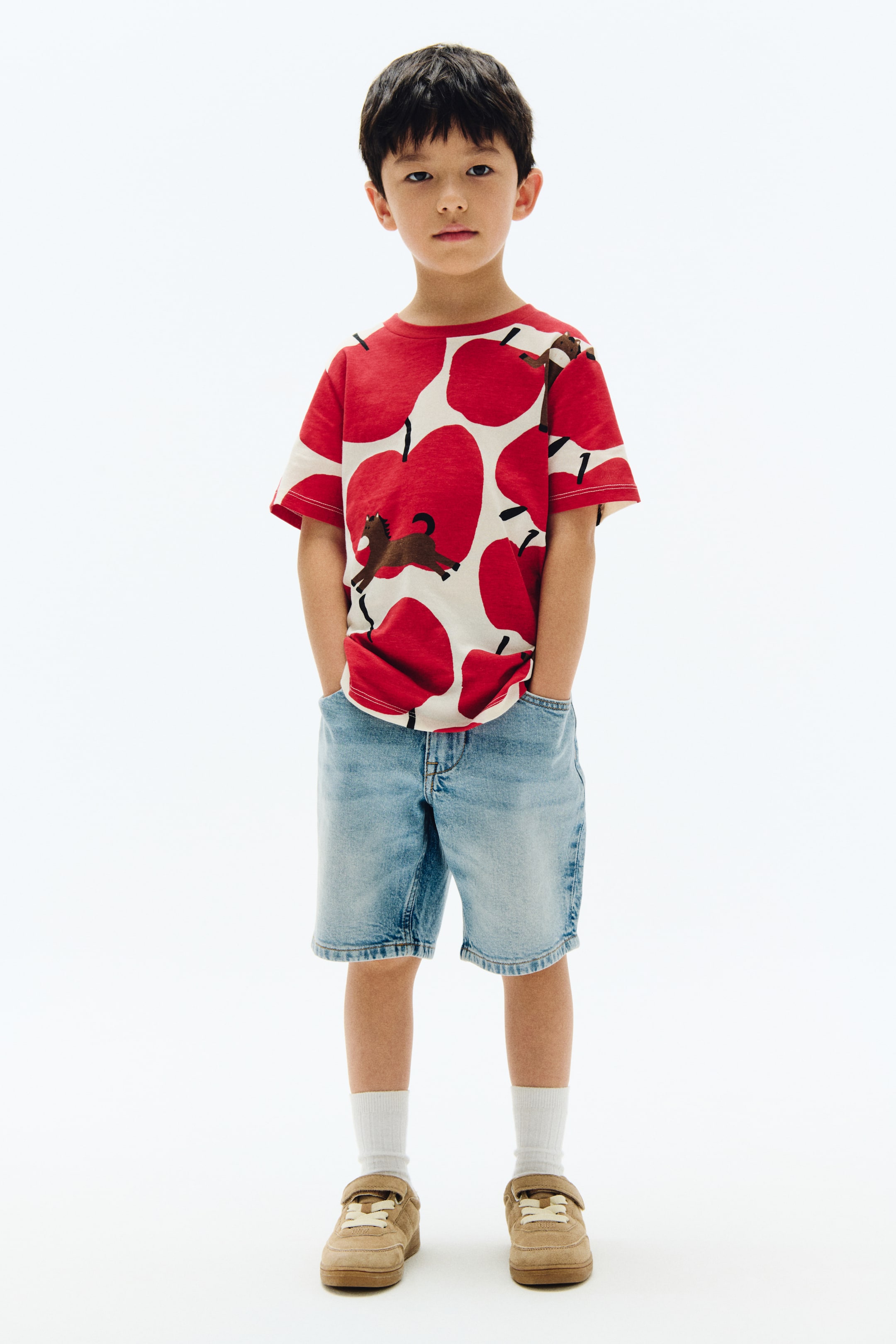 View larger image: A short-sleeved T-shirt with an all-over print of large red apples and small brown horses on a white base. Designed with a classic crew neck and short sleeves.