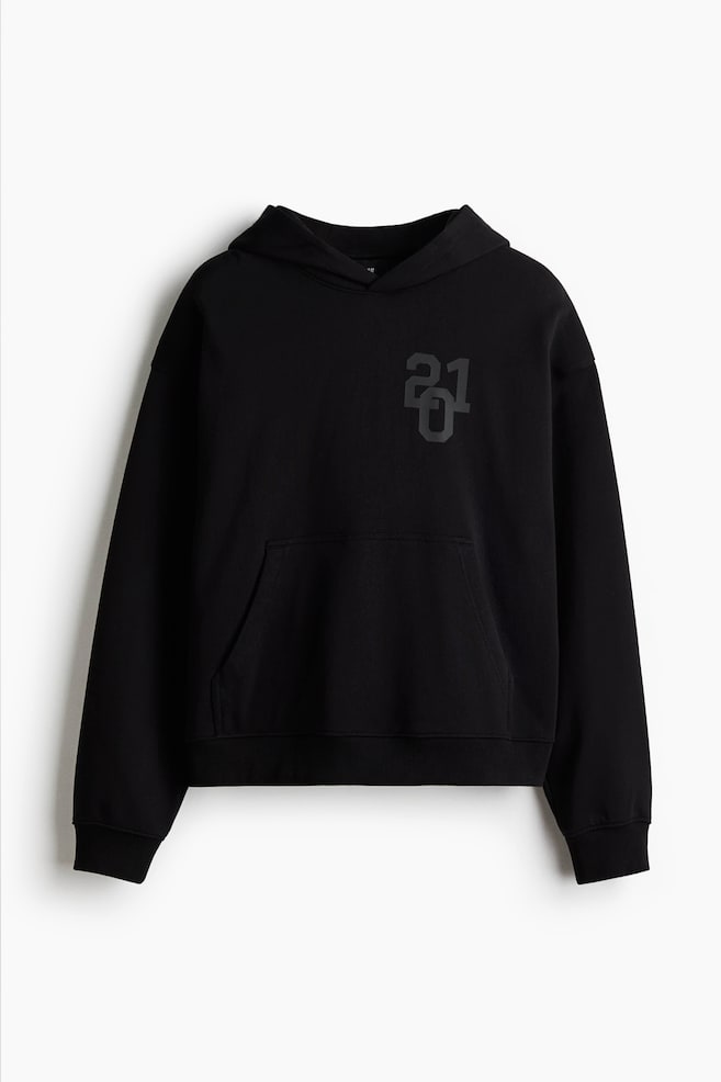 Ein schwarzer Hoodie präsentiert seine Vorderseite mit einer übergroßen, weiten Silhouette, die eine doppellagige Kapuze, tief fallende Schultern, lange Ärmel, eine Kängurutasche, gerippte Bündchen und einen gerippten Saum aufweist. Ein dunkelgraues „201“-Grafik ist auf der linken Brust sichtbar. - 1