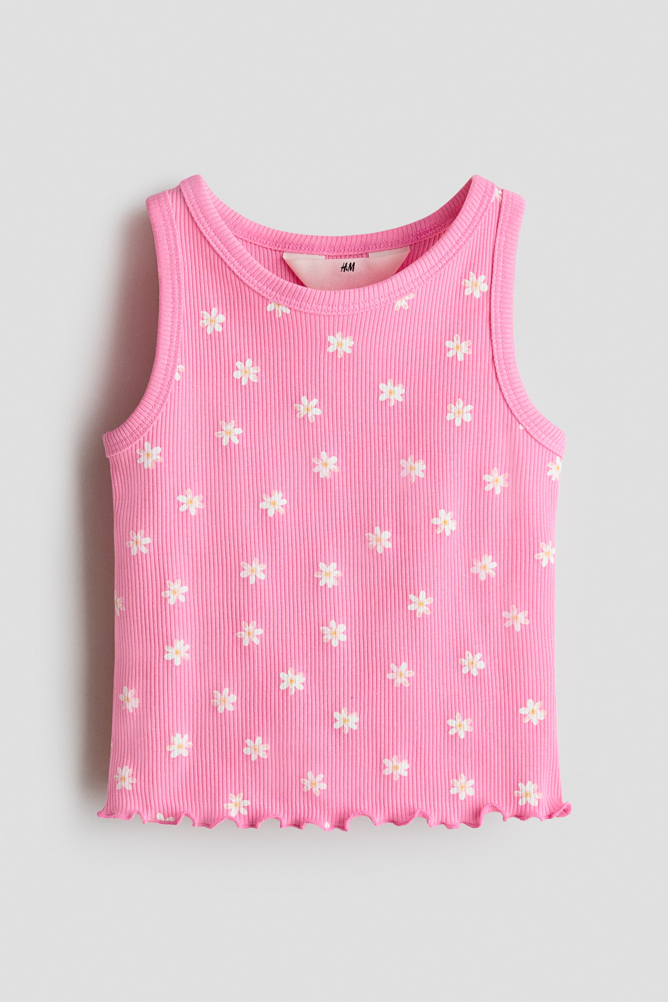 View larger image: A pink ribbed tank top showcases its front, adorned with a pattern of small white daisies with yellow centers all over. It features a round neckline, neatly trimmed armholes, and a scalloped lettuce-edge hem.