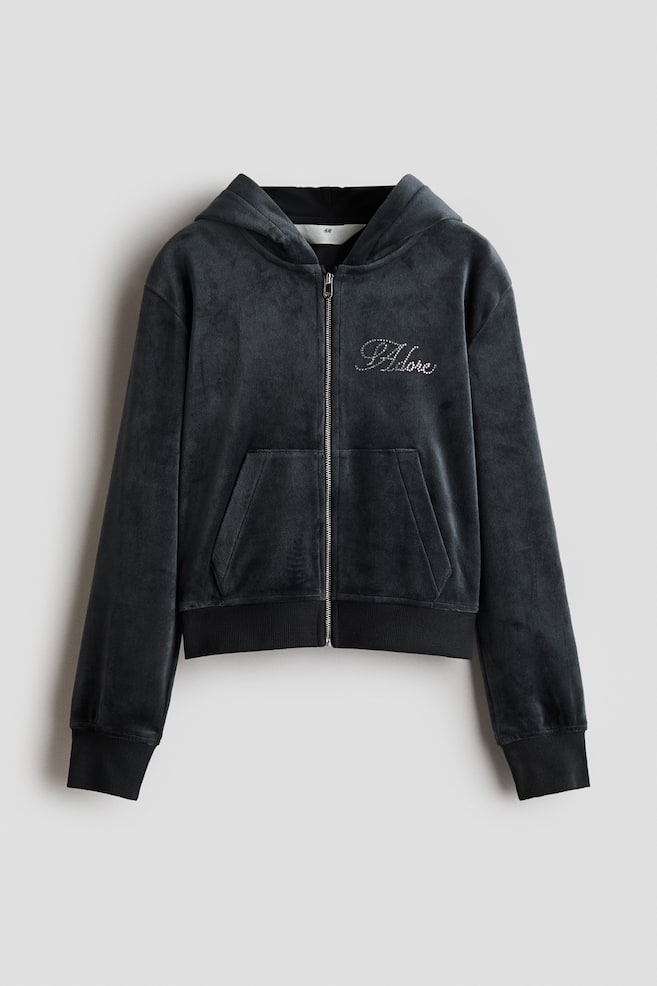 A dark grey velour zip-up hoodie is shown from the front, featuring an attached hood, a full-length front zipper, and a split kangaroo pocket. Rhinestone-embellished cursive script details the left chest, while ribbed knit bands finish the cuffs and hem. - 1