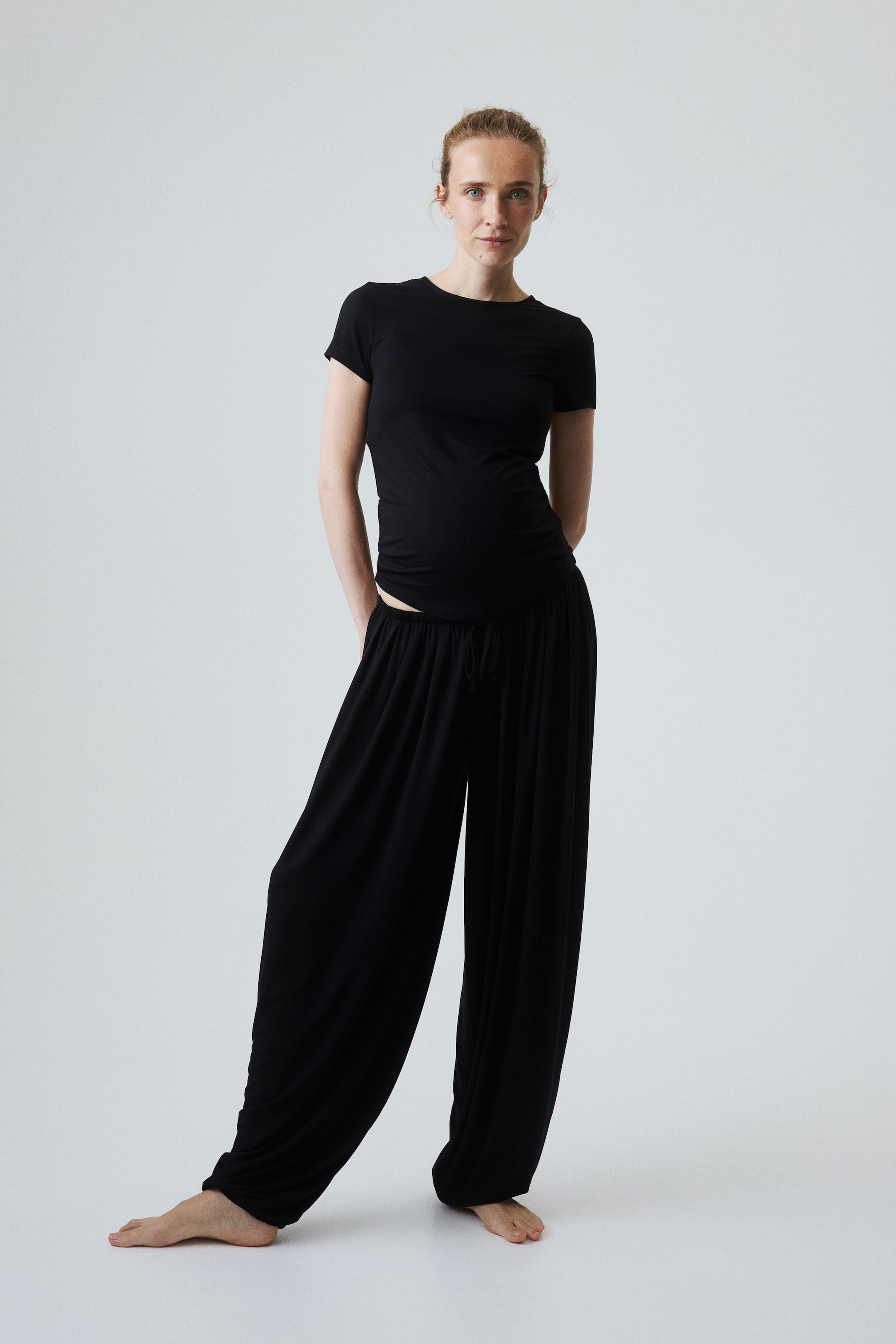 View larger image: The model is wearing a black fitted short-sleeved T-shirt. Black wide-leg trousers with a visible drawstring waistband are also worn, featuring a relaxed drape that pools at the ankles.