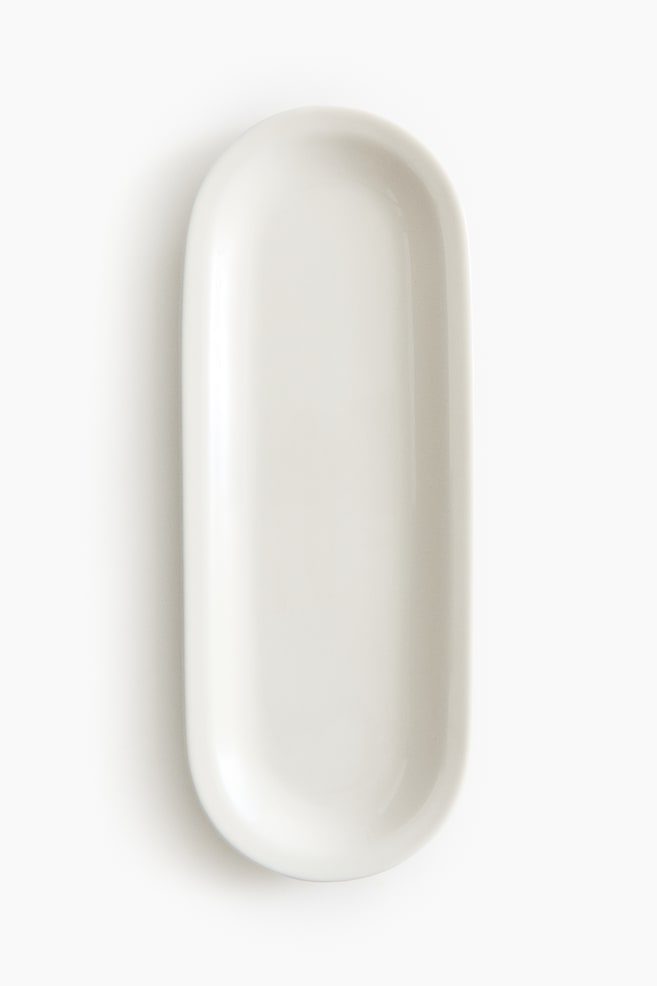 A white, glossy, elongated oval dish is featuring a shallow well and slightly raised edges. It is showing rounded ends while being viewed from directly above. - 1