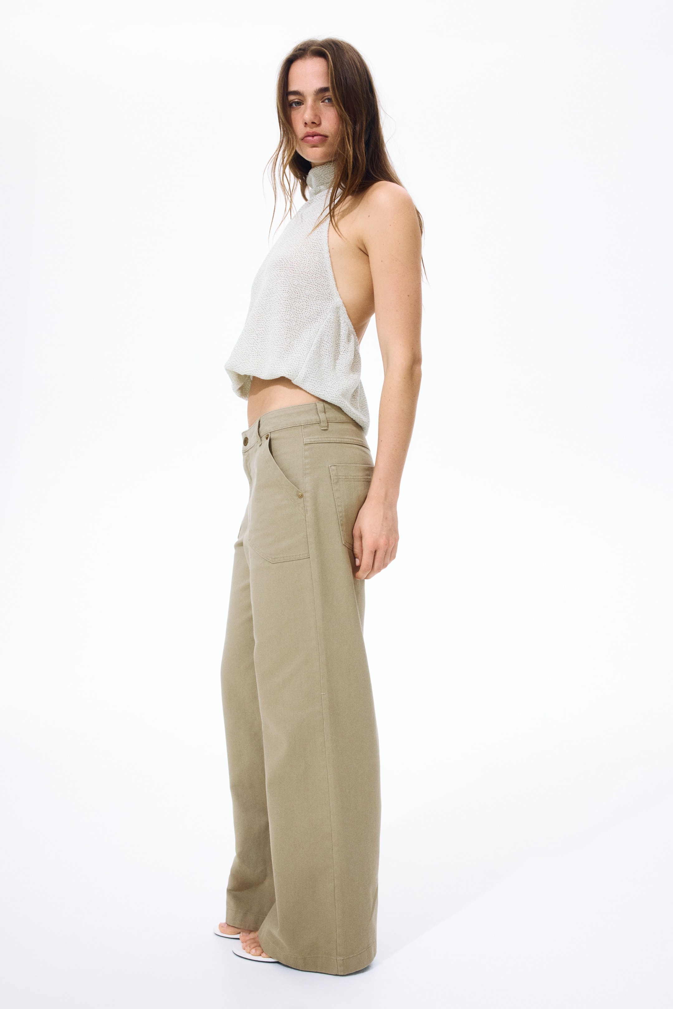 View larger image: Khaki cotton twill pants feature a high waist with a zip fly and button closure. They present patch side pockets and wide legs, viewed from a slightly right-facing angle.