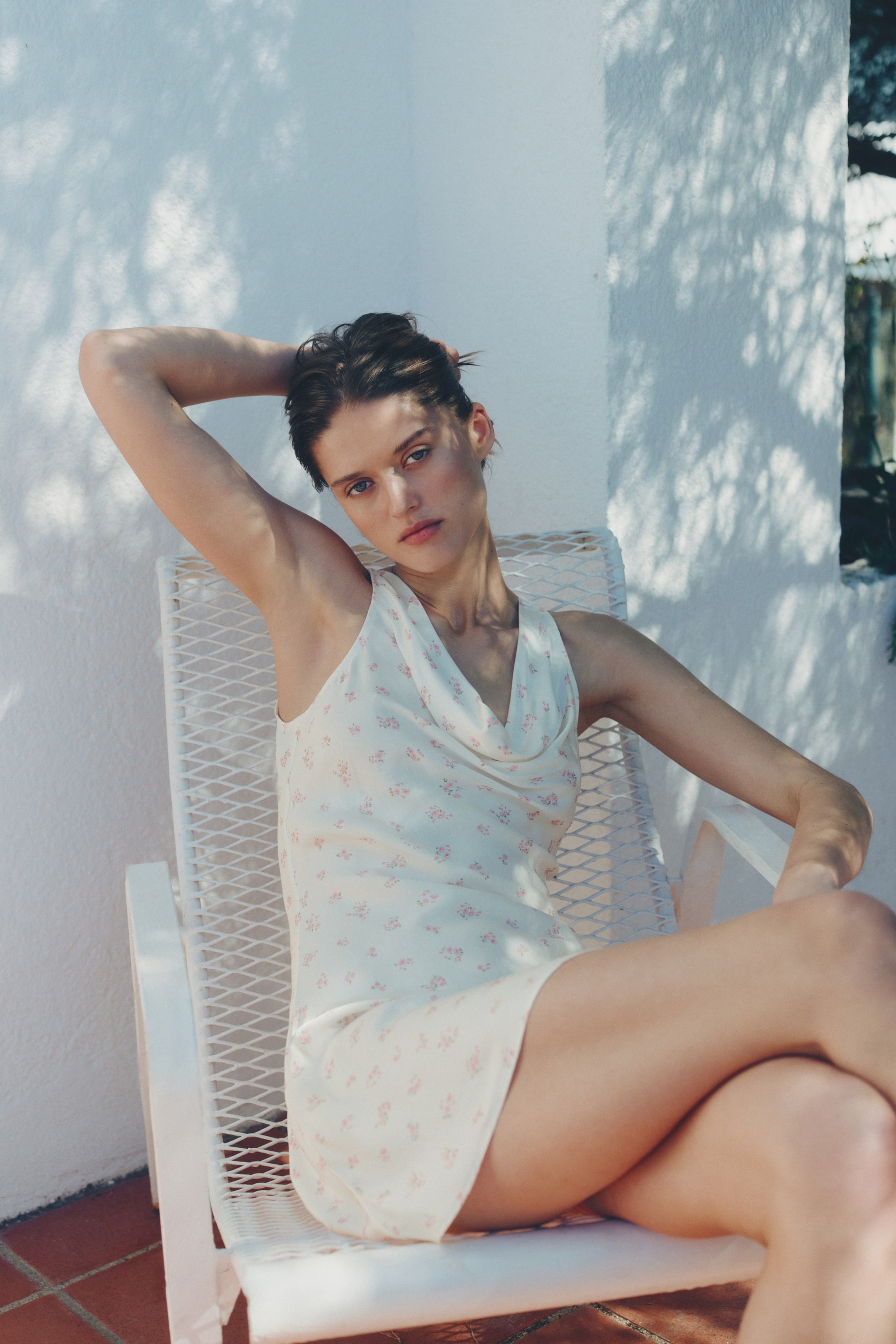 View larger image: This sleeveless mini dress features a cowl neck and is crafted from a light cream fabric adorned with a delicate pink floral print. The dress drapes elegantly on the figure from a front-facing angle, highlighting its relaxed fit.
