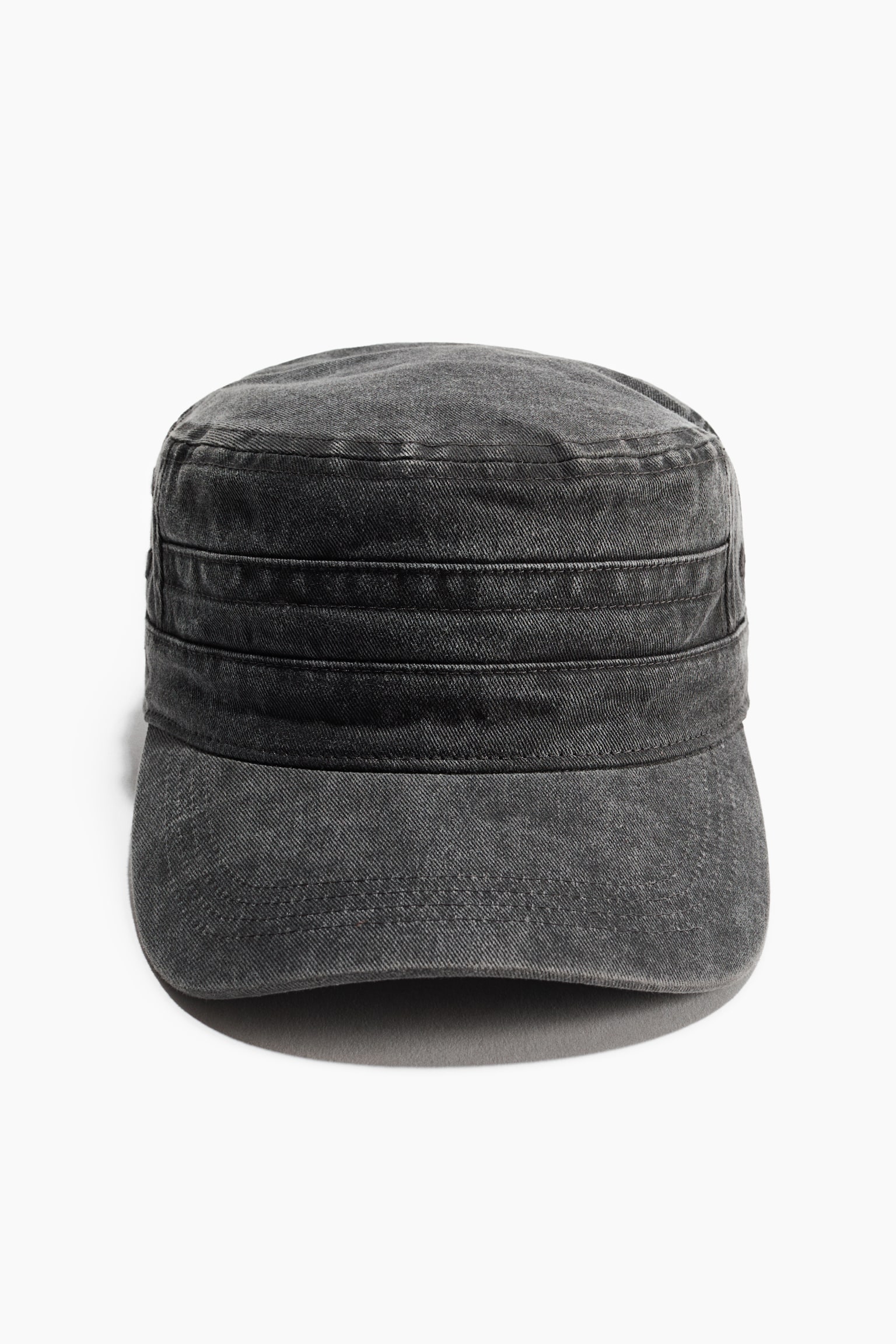 Ciemnoszara czapka typu cadet z wypranego denimu jest skierowana przodem, prezentując płaską koronę oraz usztywnianą, cylindryczną konstrukcję. Czapka ma poziome, przeszywane panele wokół otoku oraz zakrzywiony daszek z widocznymi przeszyciami wierzchnimi.