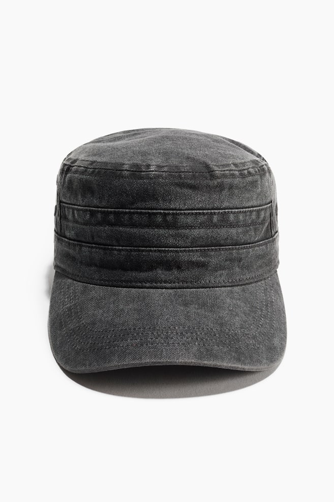 A dark grey washed-denim cadet cap is facing front, displaying a flat-topped crown and a structured cylindrical design. The cap is featuring horizontal stitched panels around the band and a curved brim with visible topstitching. - 1
