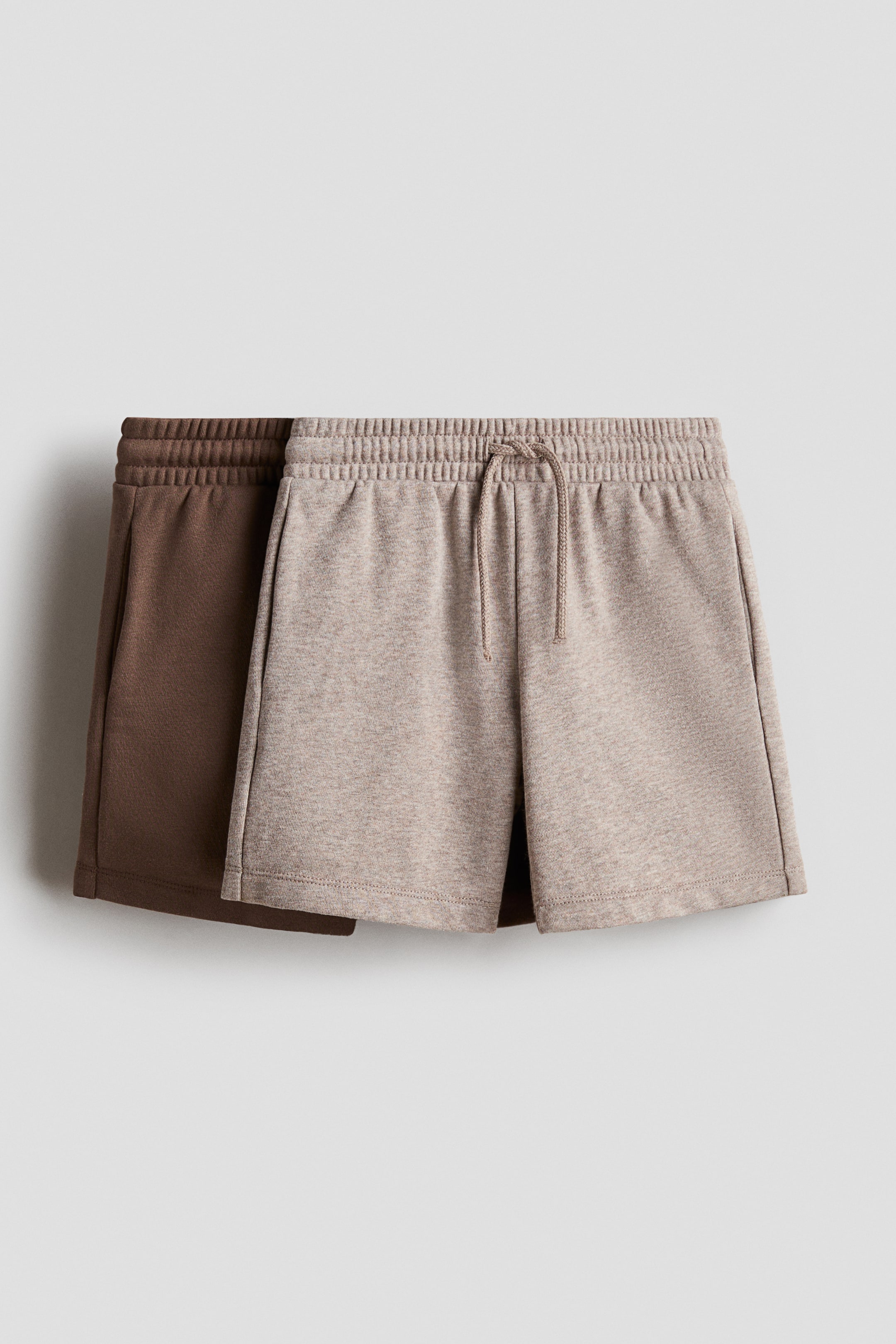 View larger image: "Presenting a duo of sweatshirt fabric shorts. The front pair, in a light heathered beige shade, showcases an elasticated waist with a drawstring and subtle side pockets, while the solid brown pair is layered in the background."
