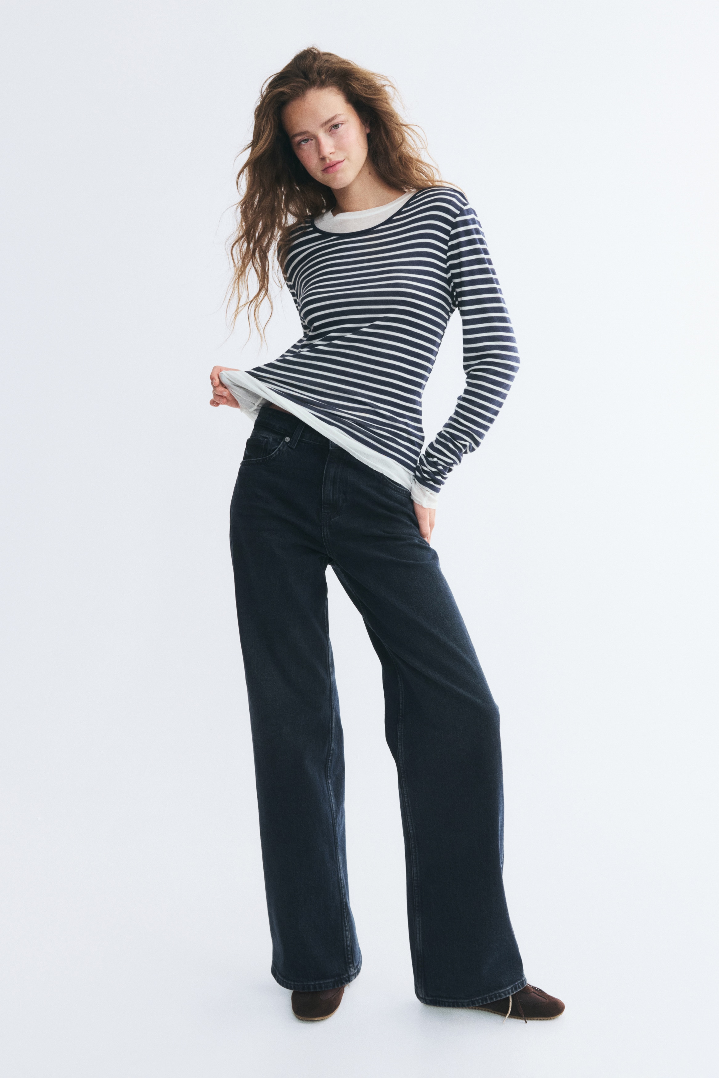 A pair of dark blue, high-waisted denim jeans is shown from the front, featuring a classic five-pocket design with a button fastening and zip fly. The jeans have a regular fit from the waist to the hips, which transitions into a loose, straight-leg cut.