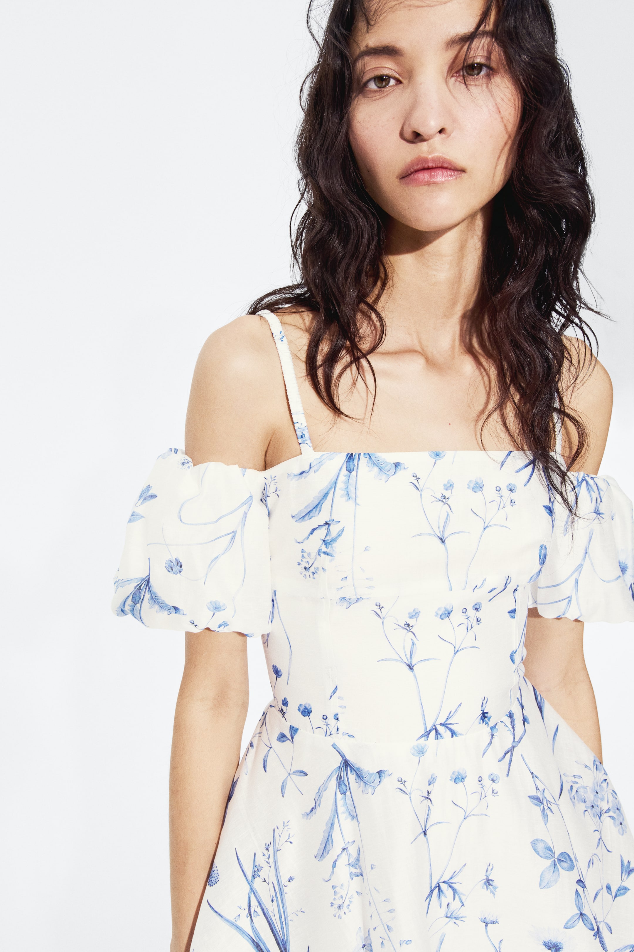 Ampliar la imagen: La modelo lleva puesto un vestido con estampado floral azul, que presenta un escote recto, tirantes delgados, mangas abullonadas al hombro, un corpiño ajustado con costura bajo el busto y una falda acampanada.