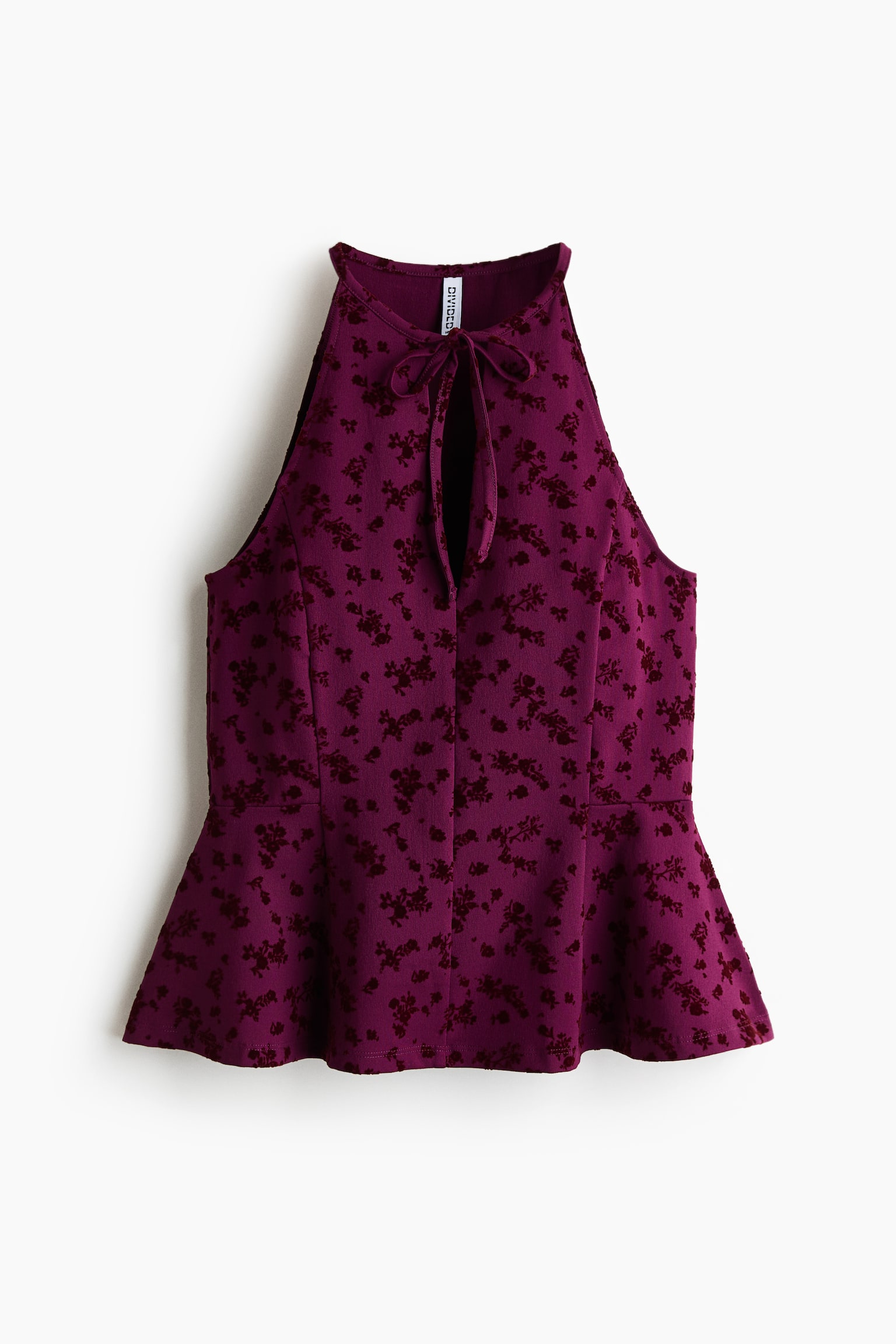 A front view showing a dark purple sleeveless jersey top featuring an all-over dark red flock floral print. The top is designed with a high round neckline, a deep, V-shaped front opening with narrow ties, and vertical shaping seams that lead to a flared peplum hem.