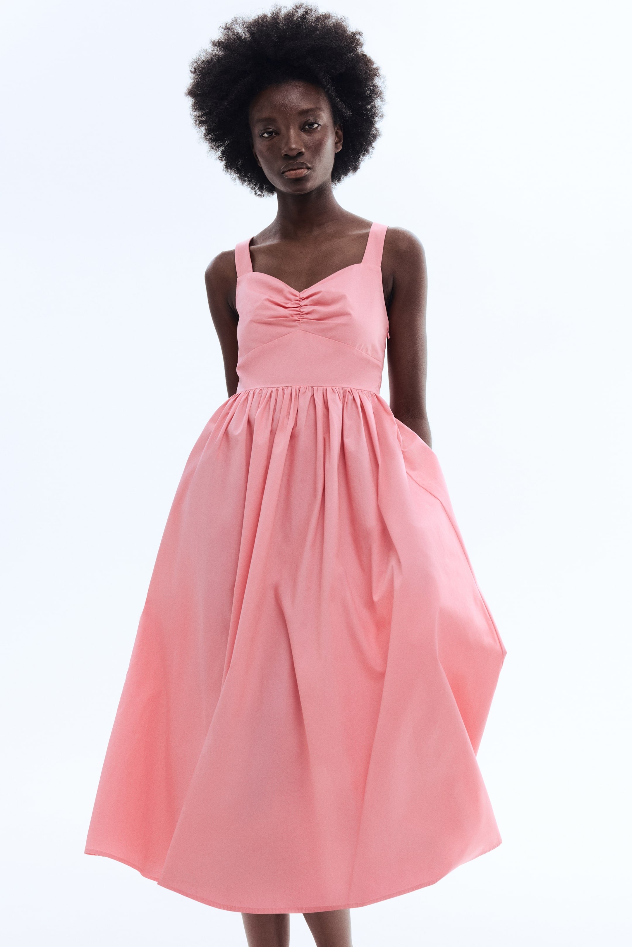 View larger image: A pink dress showcasing a sweetheart neckline with central ruching, broad shoulder straps, and a tailored waist. The voluminous, gathered skirt includes side pockets and extends to a midi length.