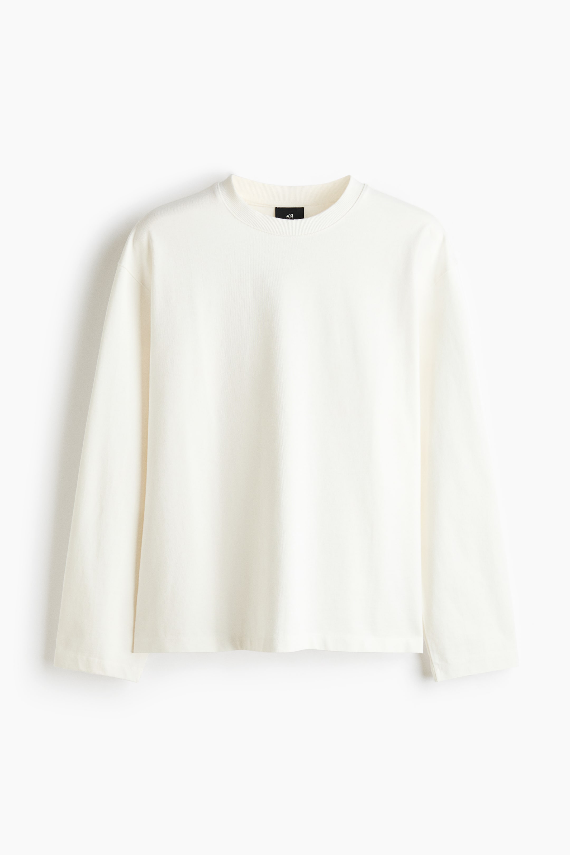View larger image: A cream long-sleeve t-shirt is showcased from the front, highlighting a ribbed crew neck, long loose sleeves, and a straight hem. A black brand tag is prominently visible at the back of the neck.