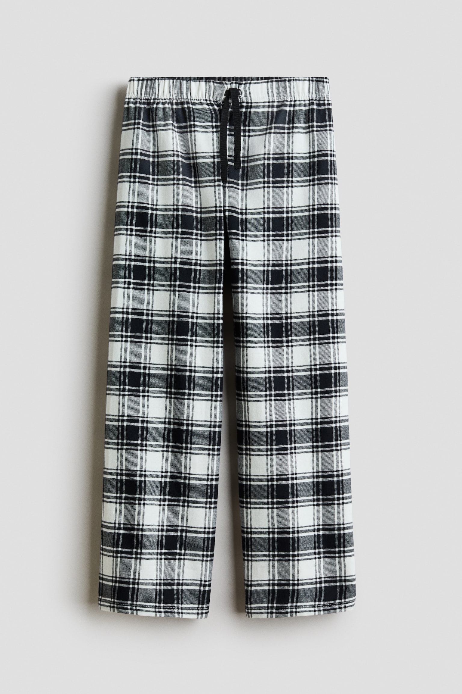 Pyjamabroek in een zwart, wit en grijs geruit patroon wordt van voren getoond, met een rechte pijp. De broek heeft een elastische tailleband met een contrasterend zwart decoratief trekkoord, in het midden gestrikt.