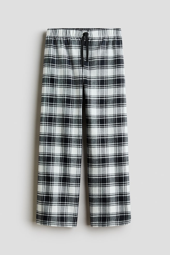 Pyjama trousers in a black, white and grey plaid pattern are shown from the front, displaying a straight-leg silhouette. The trousers feature an elasticated waistband with a contrasting black decorative drawstring tied at the centre. - 1