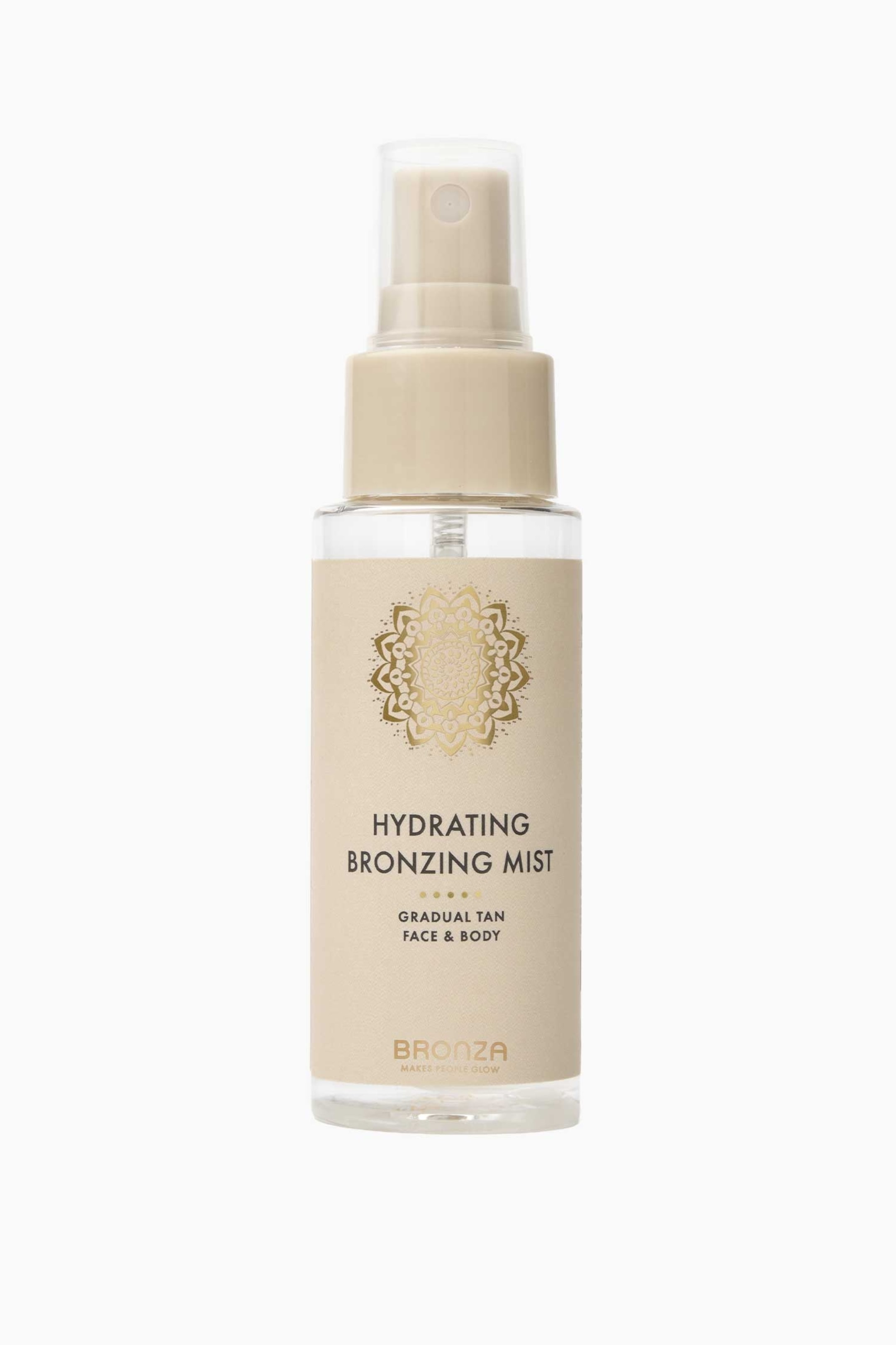 Se større billede: En klar glasflaske med fugtgivende bronzing mist står oprejst og vender fremad. Den har en beige etiket med et gyldent mandala-design og teksten "Hydrating Bronzing Mist", toppet med en beige spraypumpe og en klar beskyttelseshætte.