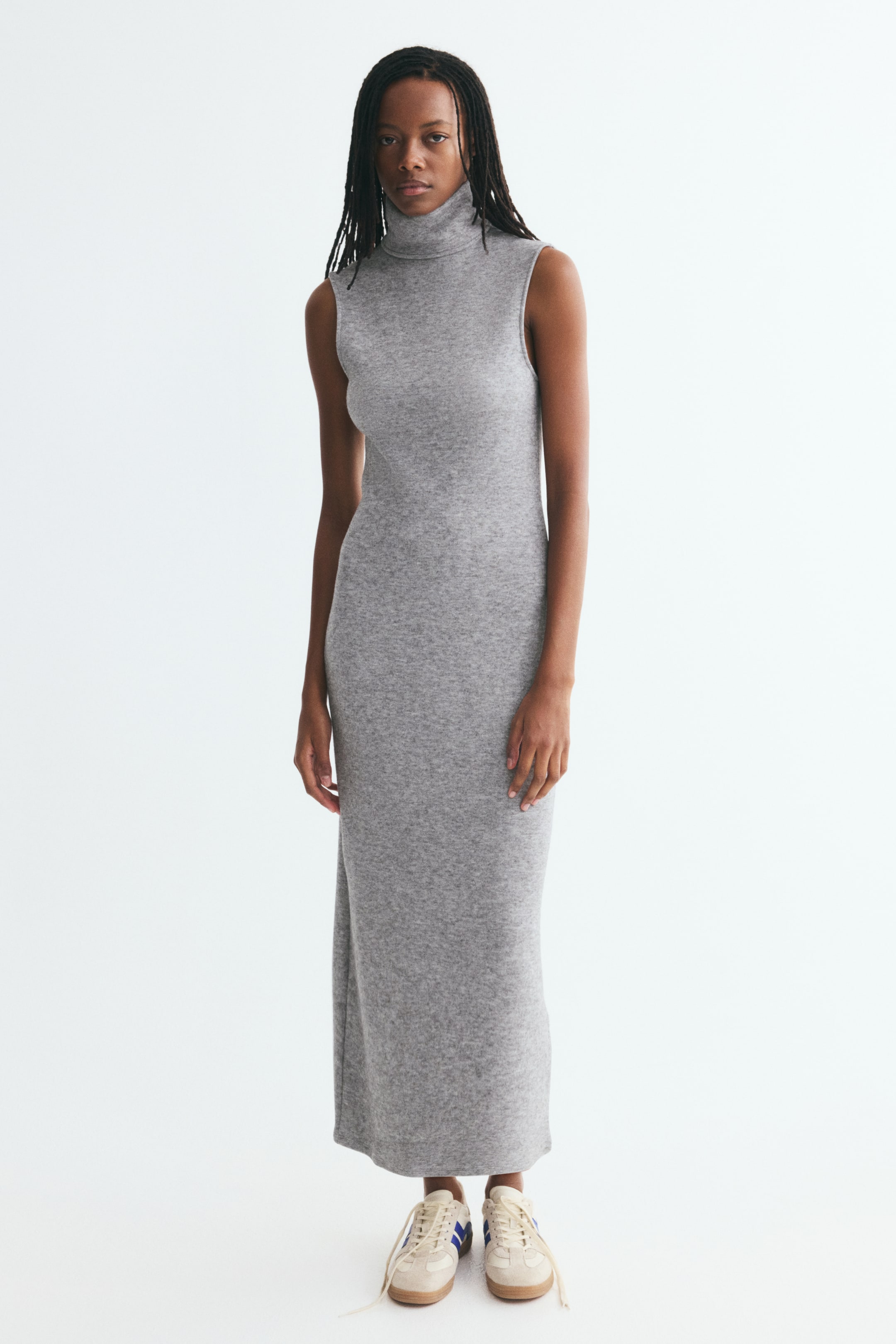 View larger image: A sleeveless light-grey knitted maxi dress is shown from the front, featuring a high turtleneck and a straight column silhouette that extends to the ankles.