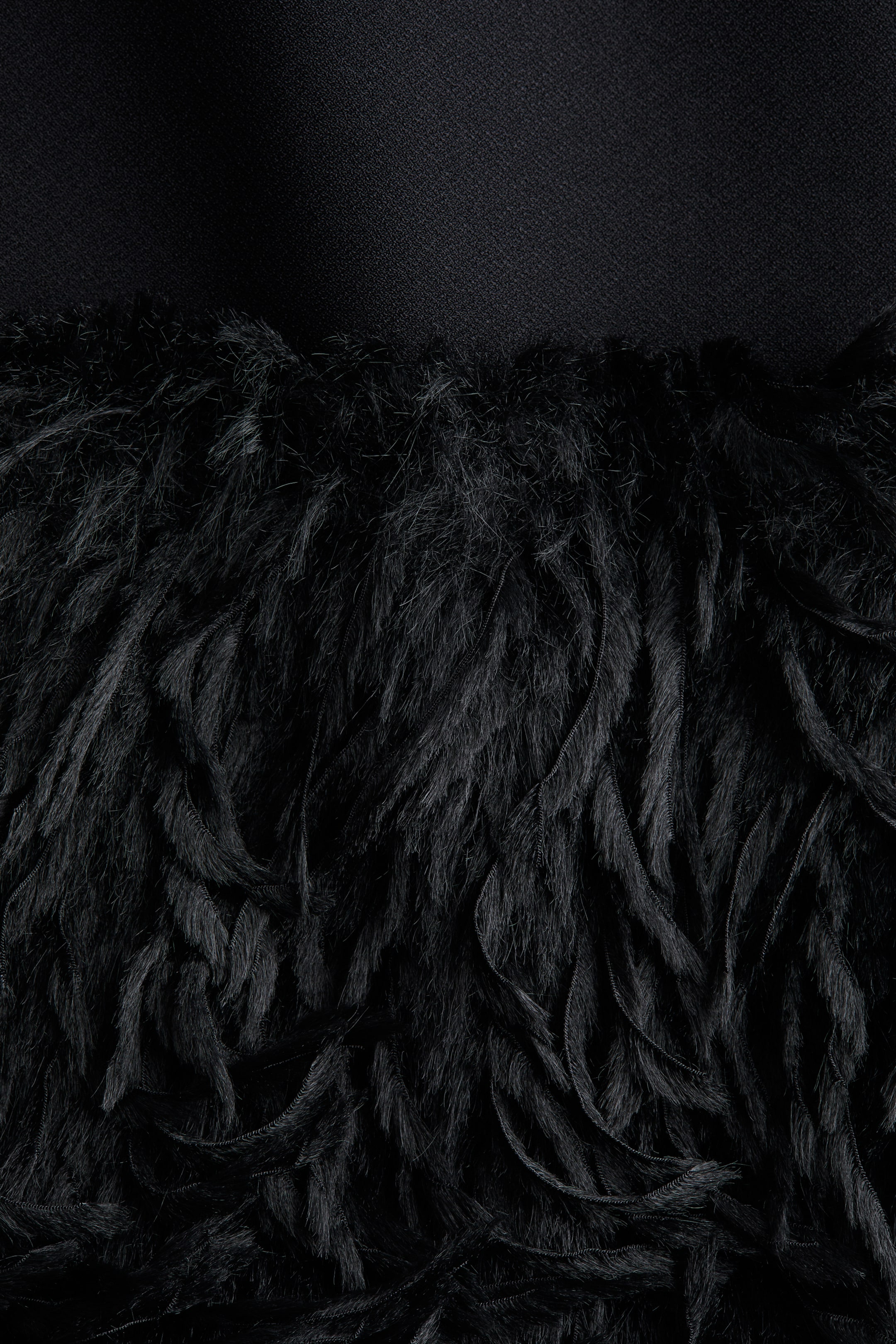 View larger image: A product detail is featuring two contrasting black fabric textures, with a smooth, tightly woven material across the top and a dense, shaggy, feather-like fabric filling the bottom.