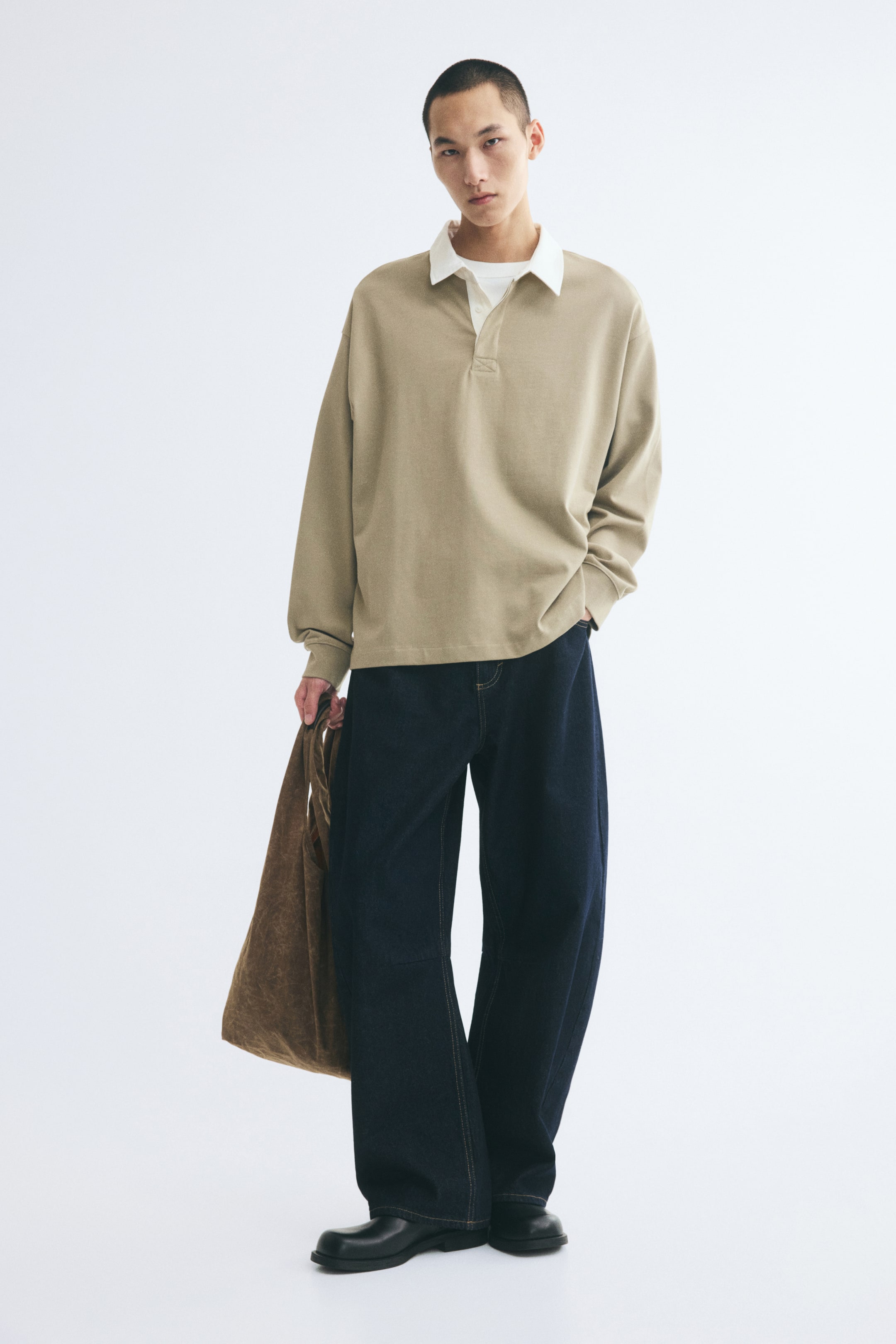 View larger image: A beige cotton-jersey rugby shirt with a contrasting white collar and a concealed button placket is worn by the model. The shirt features a relaxed fit with dropped shoulders and ribbed cuffs, and is paired with dark wide-leg jeans.