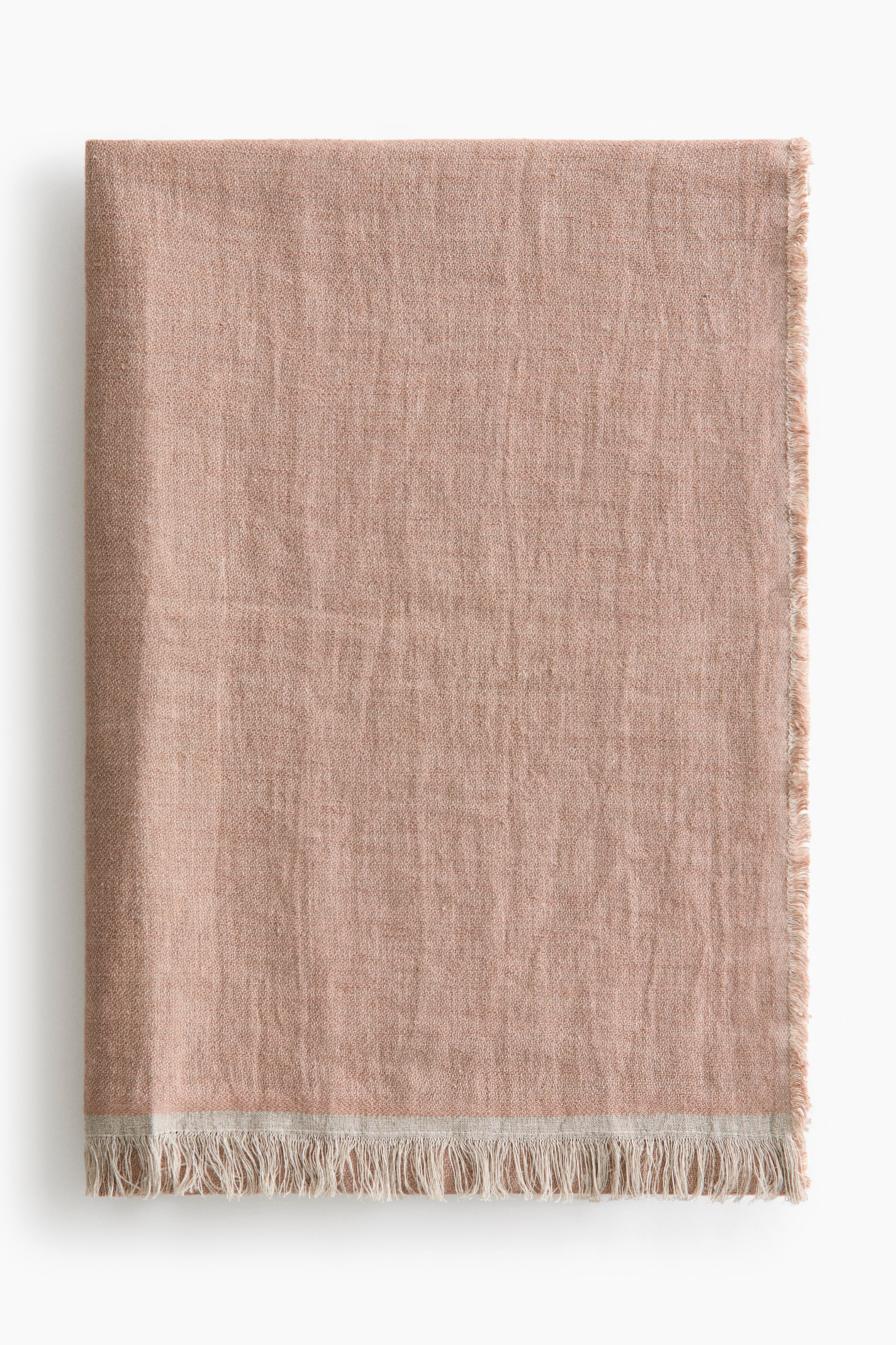 Voir une image plus grande: Une couverture rose pâle est soigneusement pliée, affichant une texture tissée avec des variations subtiles. Une bande beige clair court le long du bord inférieur, qui présente une frange effilochée, et le bord droit montre également une finition effilochée.