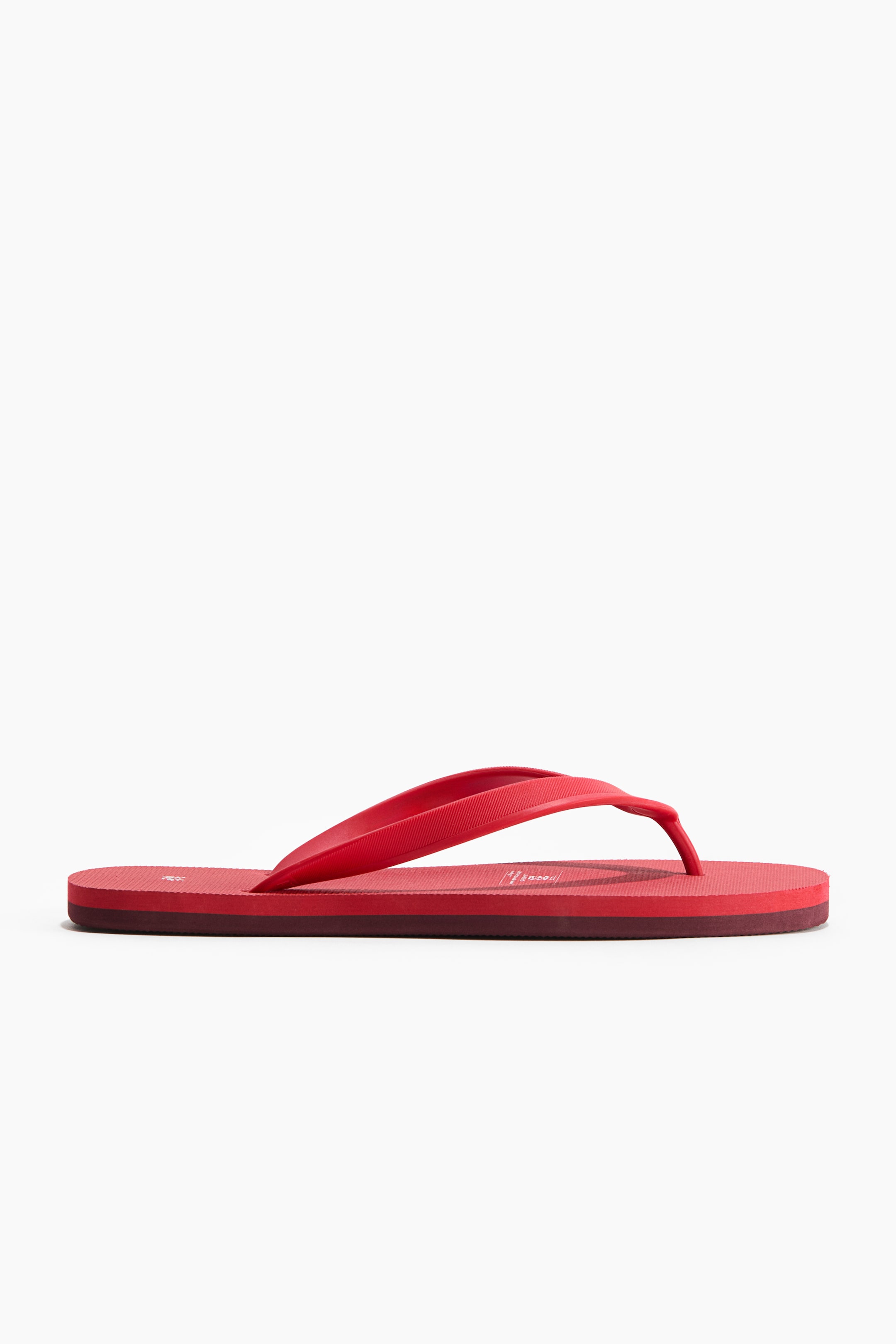 View larger image: Rubber flip-flops with straps and a slender toe post showcase a vibrant red hue. The textured straps elegantly curve over the subtly designed footbed, which boasts a multi-layered sole with a deeper red mid-layer.