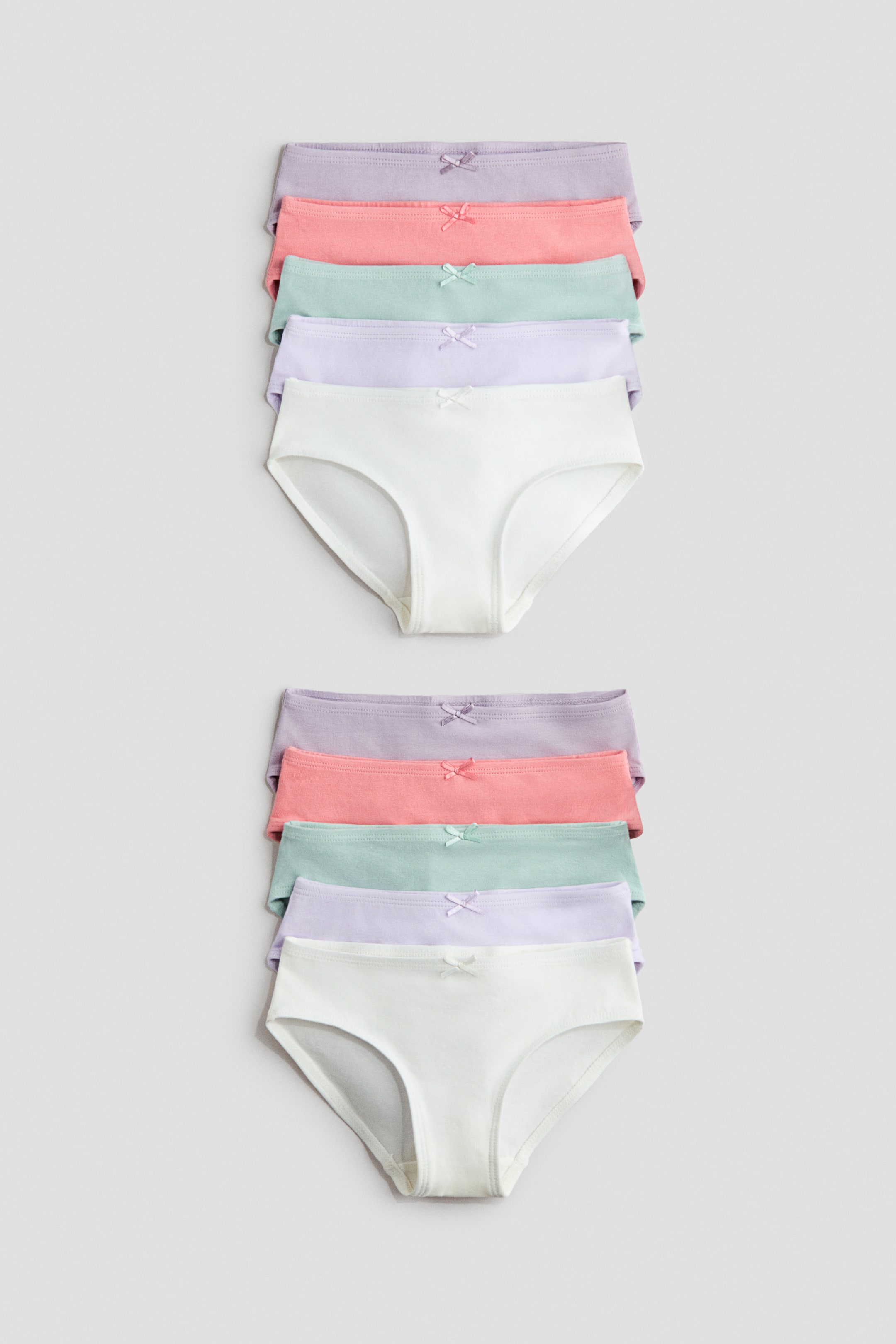 Grösseres Bild ansehen: Slips aus Baumwolljersey mit einer dekorativen Schleife vorne und einem gefütterten Zwickel werden in zwei Stapeln zu je fünf präsentiert. Jeder Slip zeigt ein frontales Design in Pastellfarben, darunter Weiß, Helllavendel, Mintgrün, Koralle und Flieder.