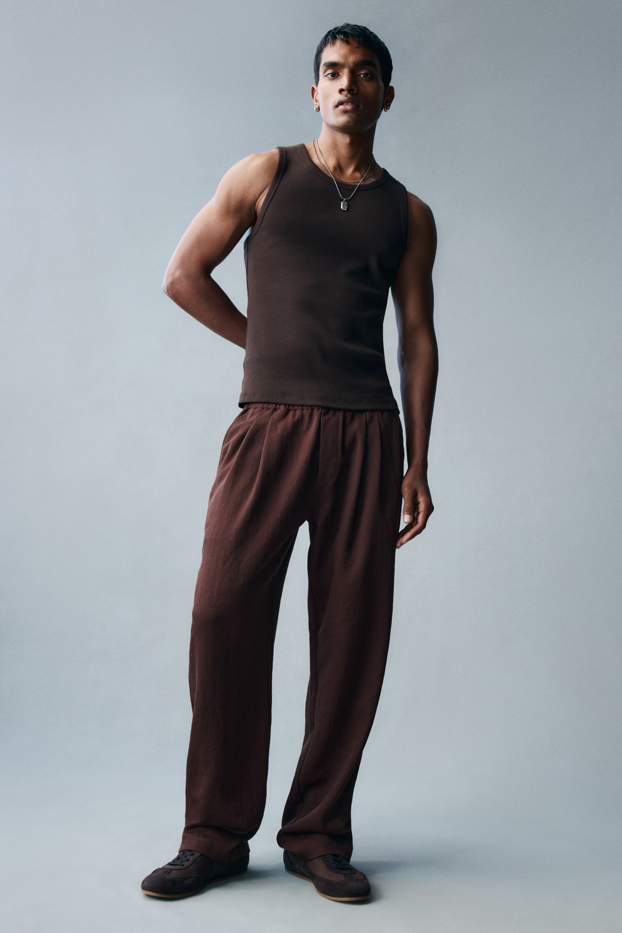 View larger image: The model is wearing dark brown trousers in a viscose-blend twill, featuring a relaxed fit, an elasticated waistband, and straight legs. The trousers are styled with a coordinating dark brown ribbed tank top and dark brown sneakers.