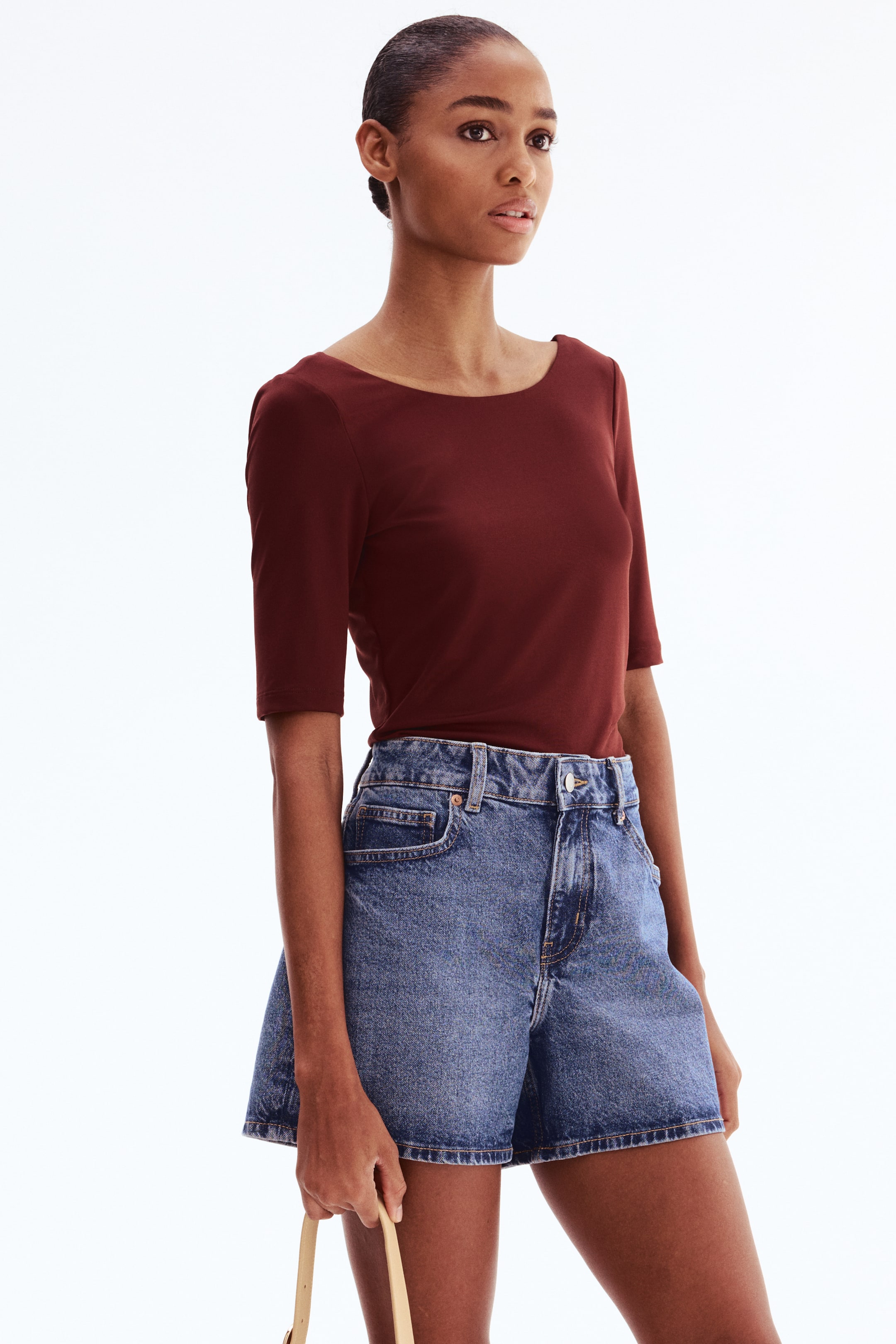 View larger image: A deep reddish-brown top features a boat neckline and elbow-length sleeves. It fits snugly on the torso and is tucked into high-waisted shorts.