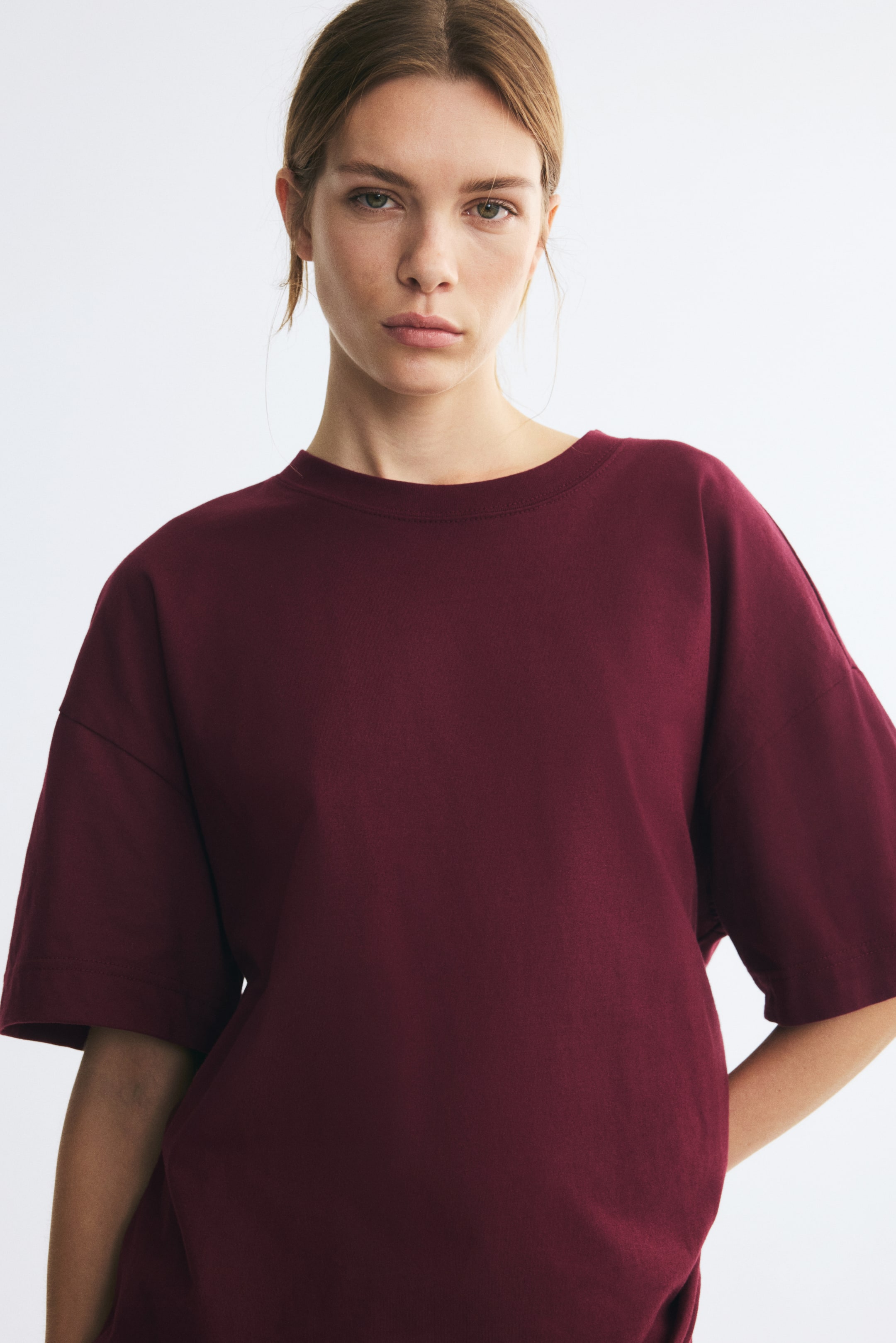 Ampliar la imagen: La modelo lleva puesta una playera extragrande color borgoña en jersey de algodón. La playera presenta cuello redondo acanalado, hombros caídos y mangas anchas y holgadas.