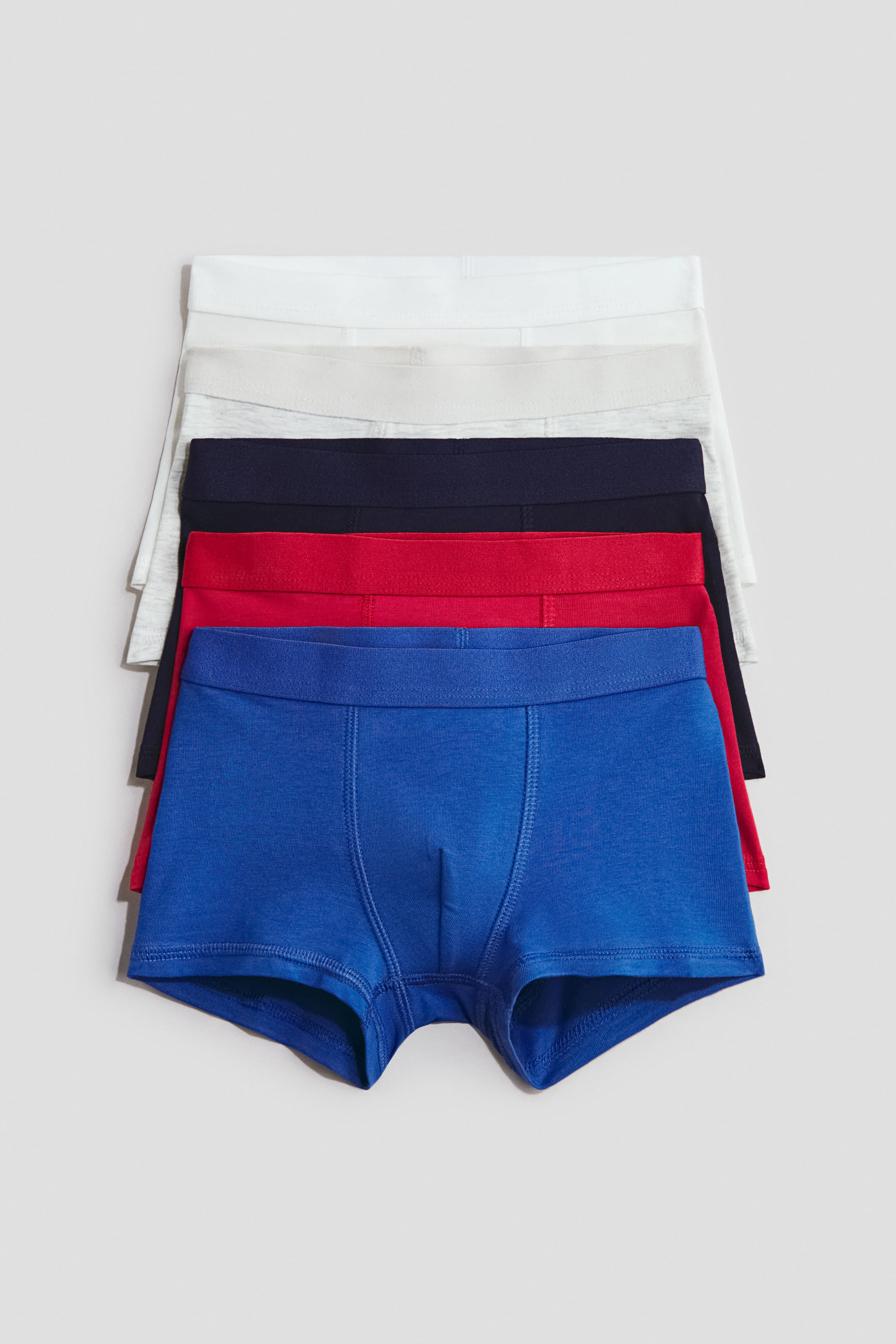 View larger image: A stack of five pairs of soft cotton jersey trunks is on display, with the blue pair at the front facing forward. Each pair features short legs, an elasticated waistband, and a lined front, available in shades of blue, red, navy, light grey marl, and white.