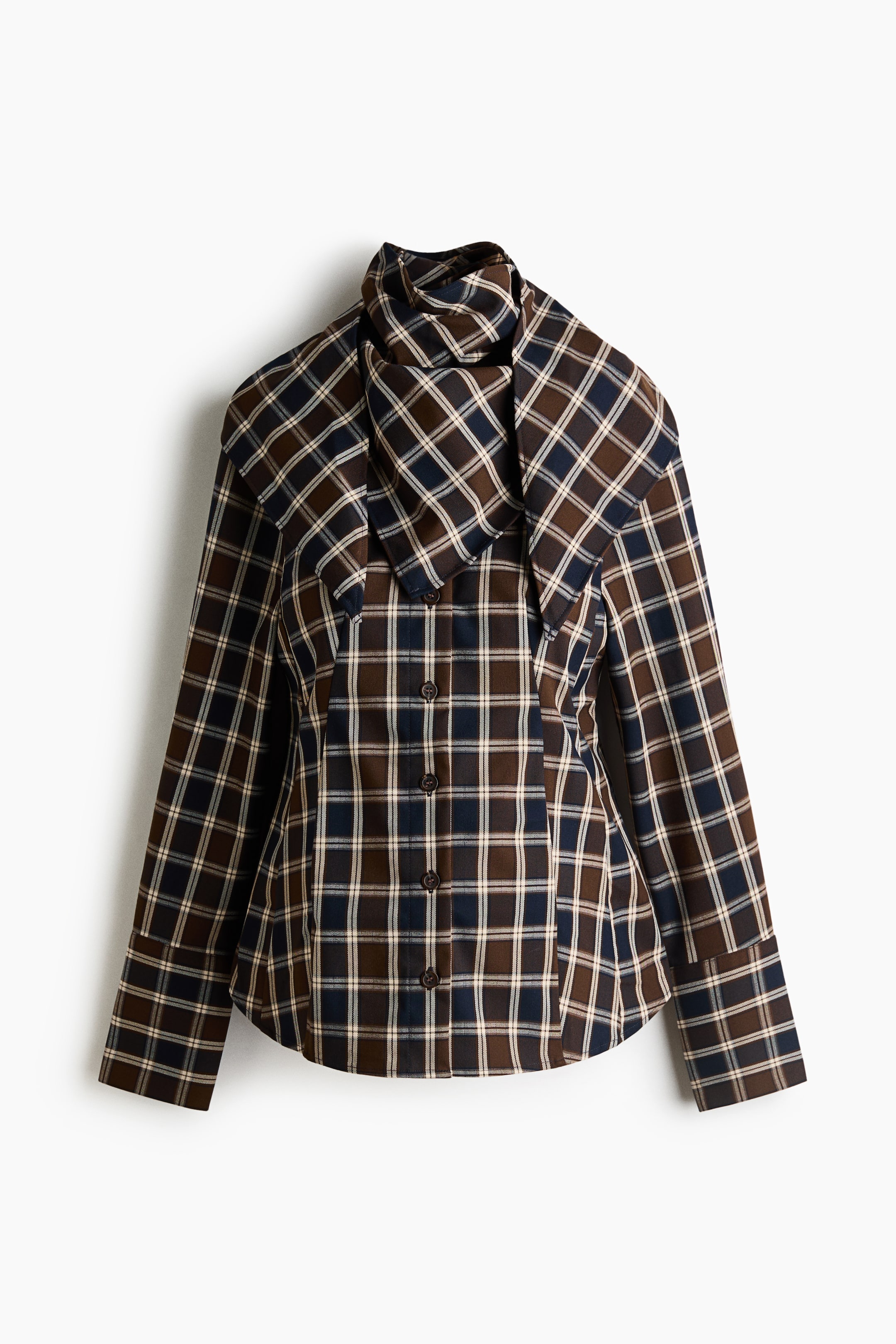 View larger image: A long-sleeve plaid shirt is shown facing front, showcasing a brown, navy blue, and white tartan pattern with a button-front closure. It features an exaggerated wide collar layered with a matching draped neck scarf and long sleeves with wide, folded cuffs.