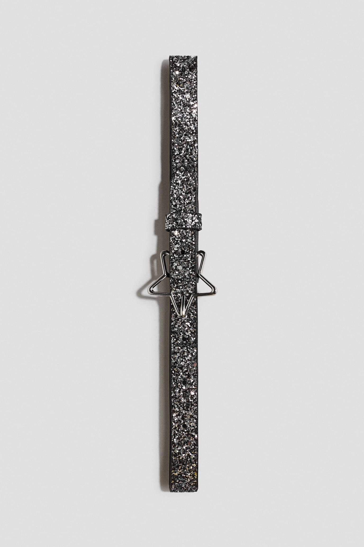 A narrow belt featuring a dark silver glitter finish is shown from the front. It features a silver-toned, star-shaped metal buckle and a matching glittery keeper loop. - 1