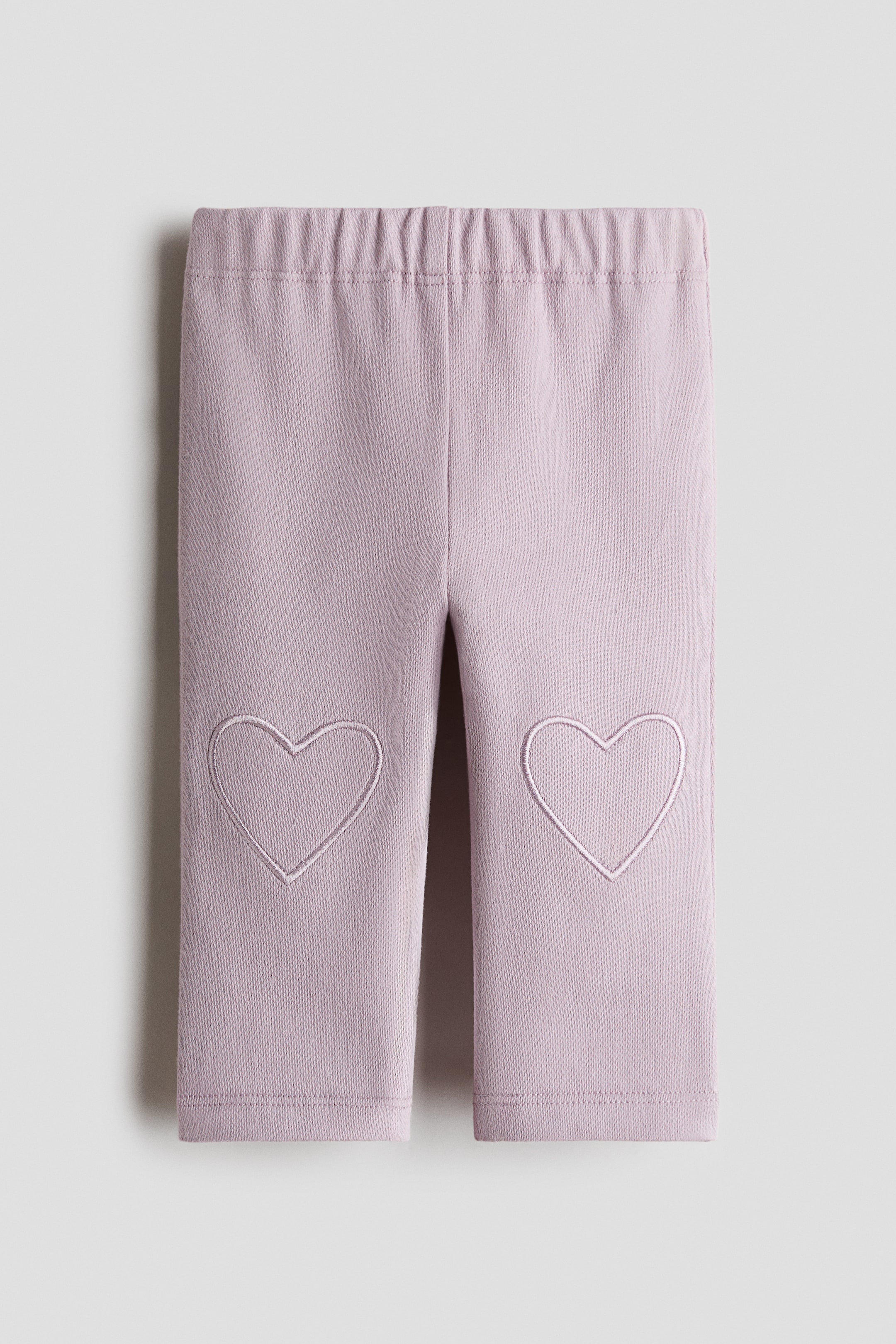 View larger image: Legging ungu muda terletak rata, dengan pinggang berelastik. Dua garisan hati bersulam kelihatan di setiap lutut, dan legging ini dilengkapkan dengan hujung yang rata.
