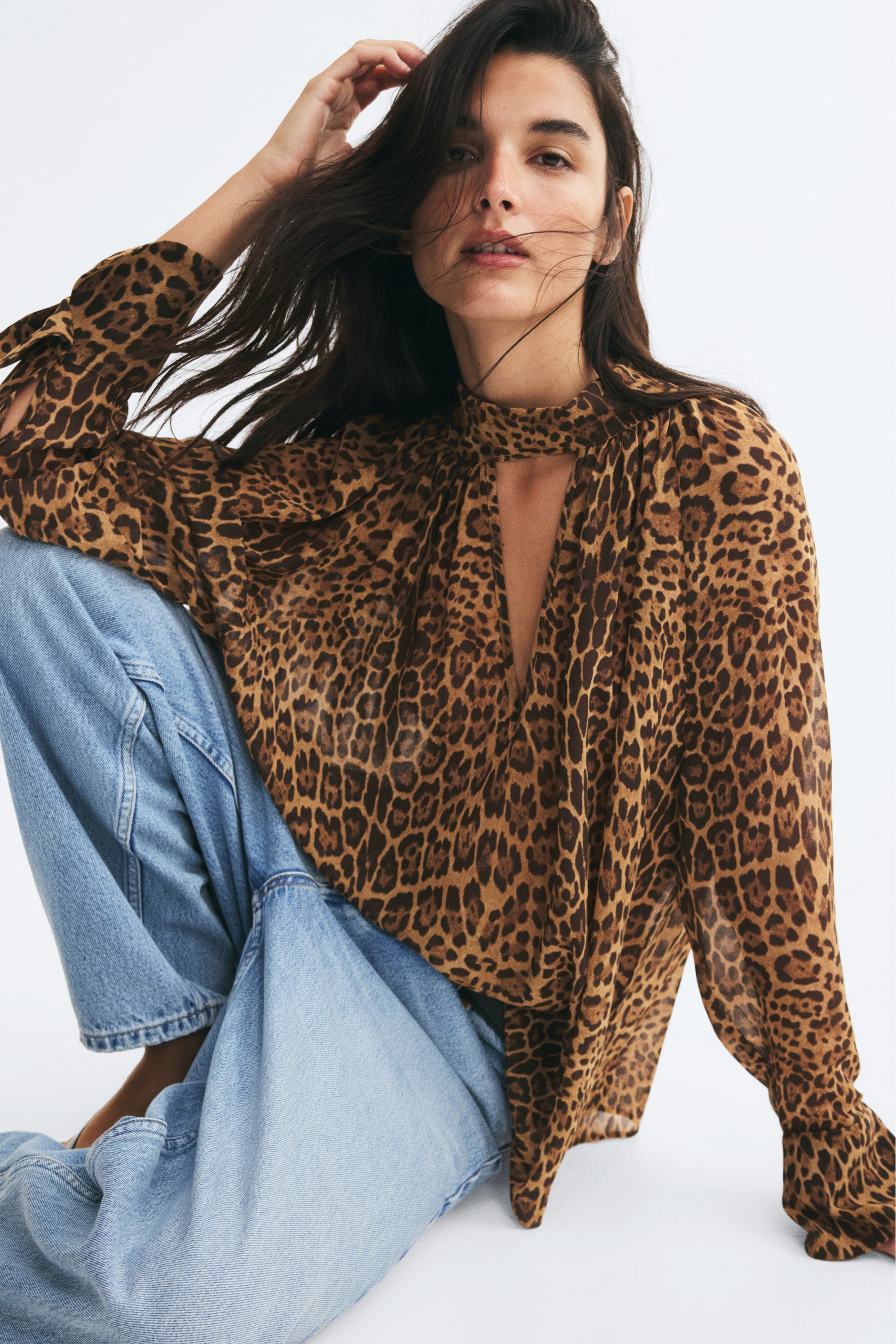 View larger image: The model is wearing an oversized, sheer leopard-print blouse, featuring a high scarf collar with a deep V-shaped front opening and long sleeves. The blouse is styled with light-blue jeans.