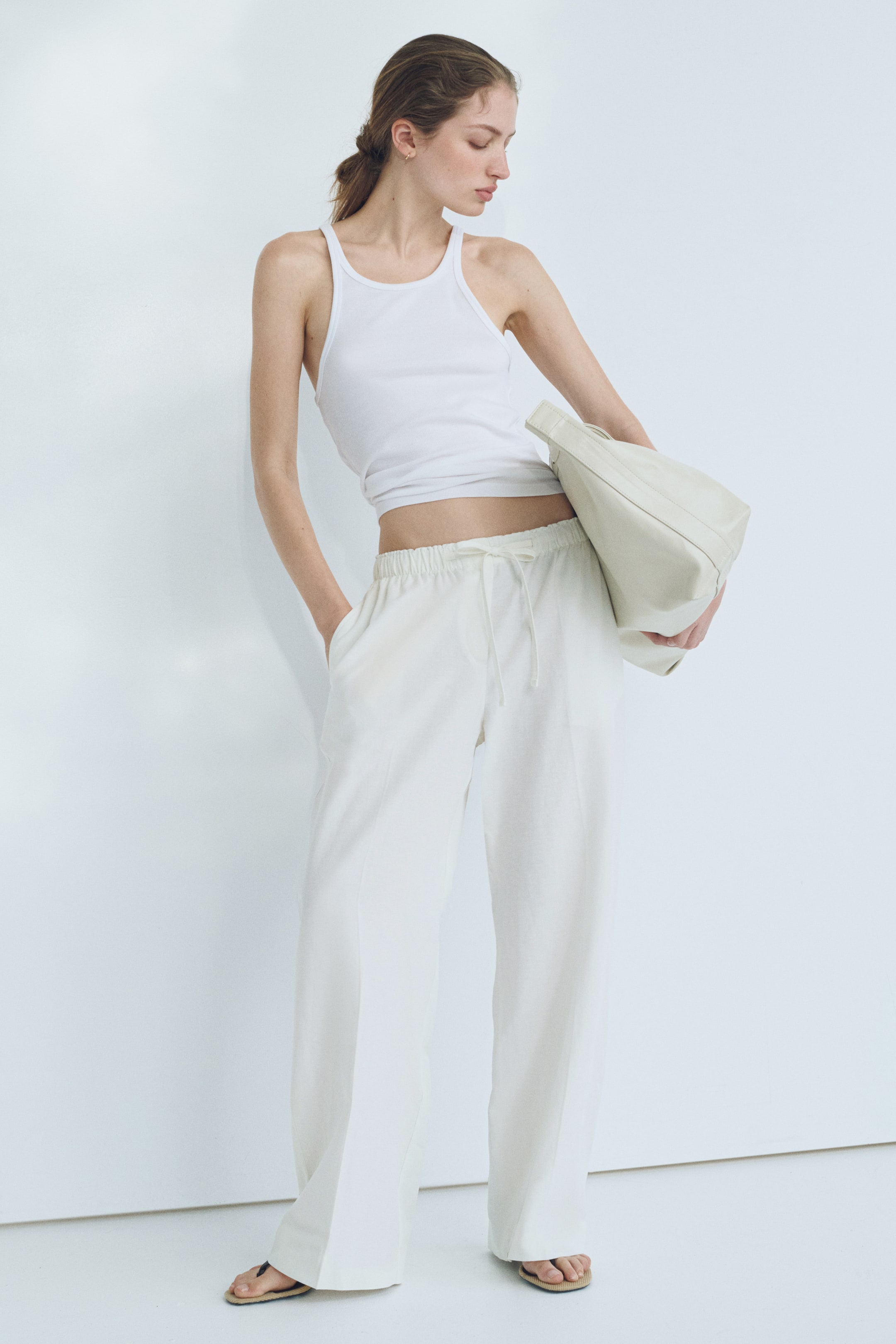 View larger image: A white ribbed tank top featuring a round neckline, broad straps, and a snug, cropped fit.