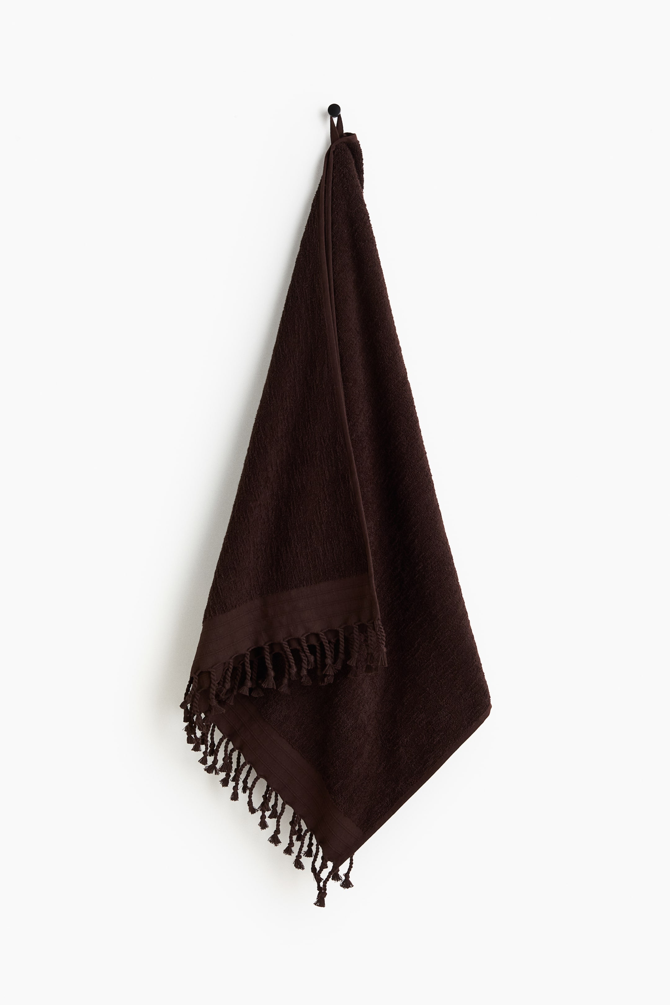 View larger image: A deep brown bath towel crafted from soft cotton terry fabric is displayed, showcasing woven ends adorned with twisted fringes along the shorter edges and a loop for hanging on one of the longer sides.