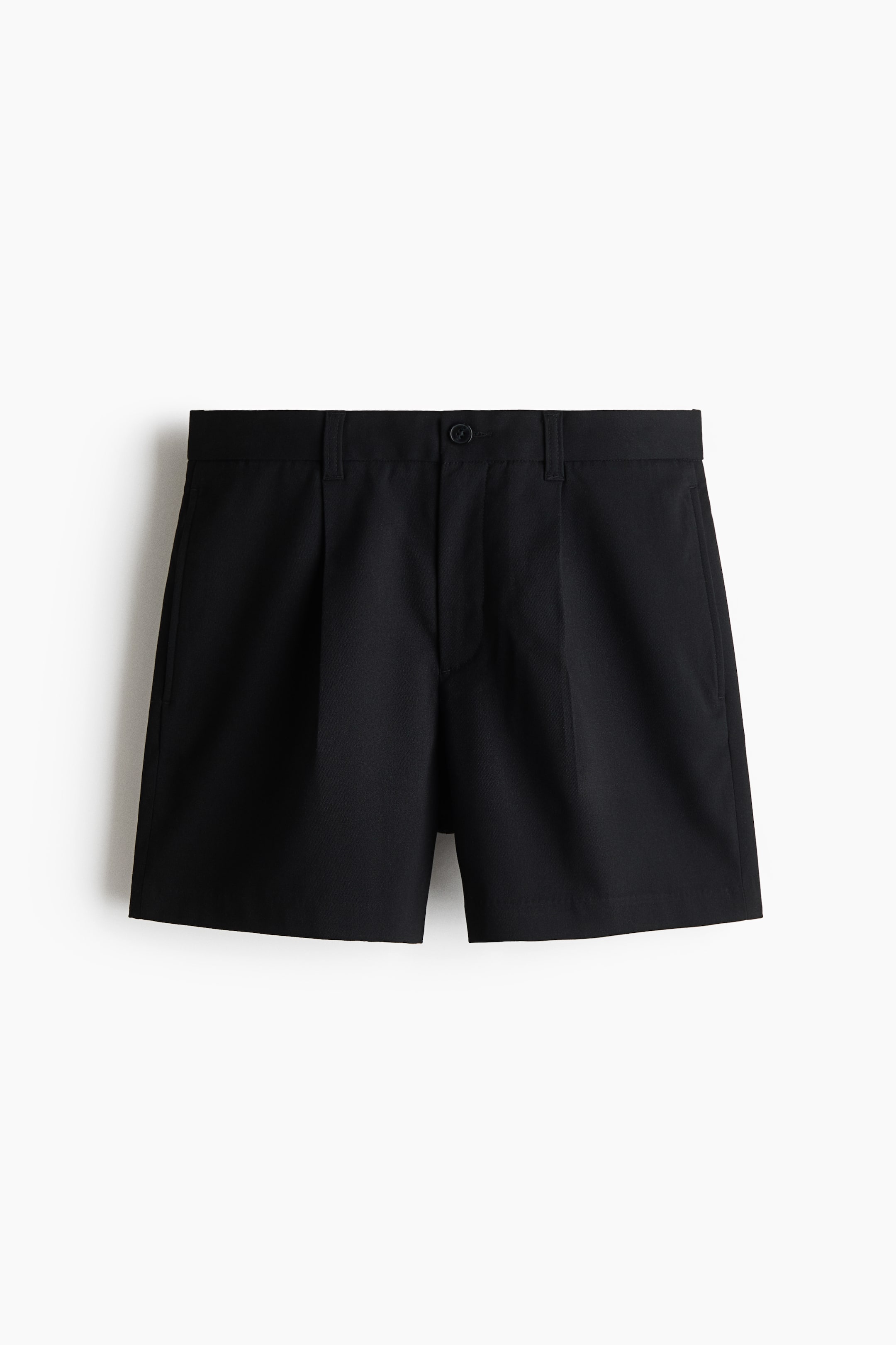 Grotere afbeelding bekijken: Zwarte shorts met een platte tailleband met riemlussen, een enkele knoopsluiting en een ritssluiting aan de voorkant, samen met naar voren gerichte plooien en schuine zijzakken.