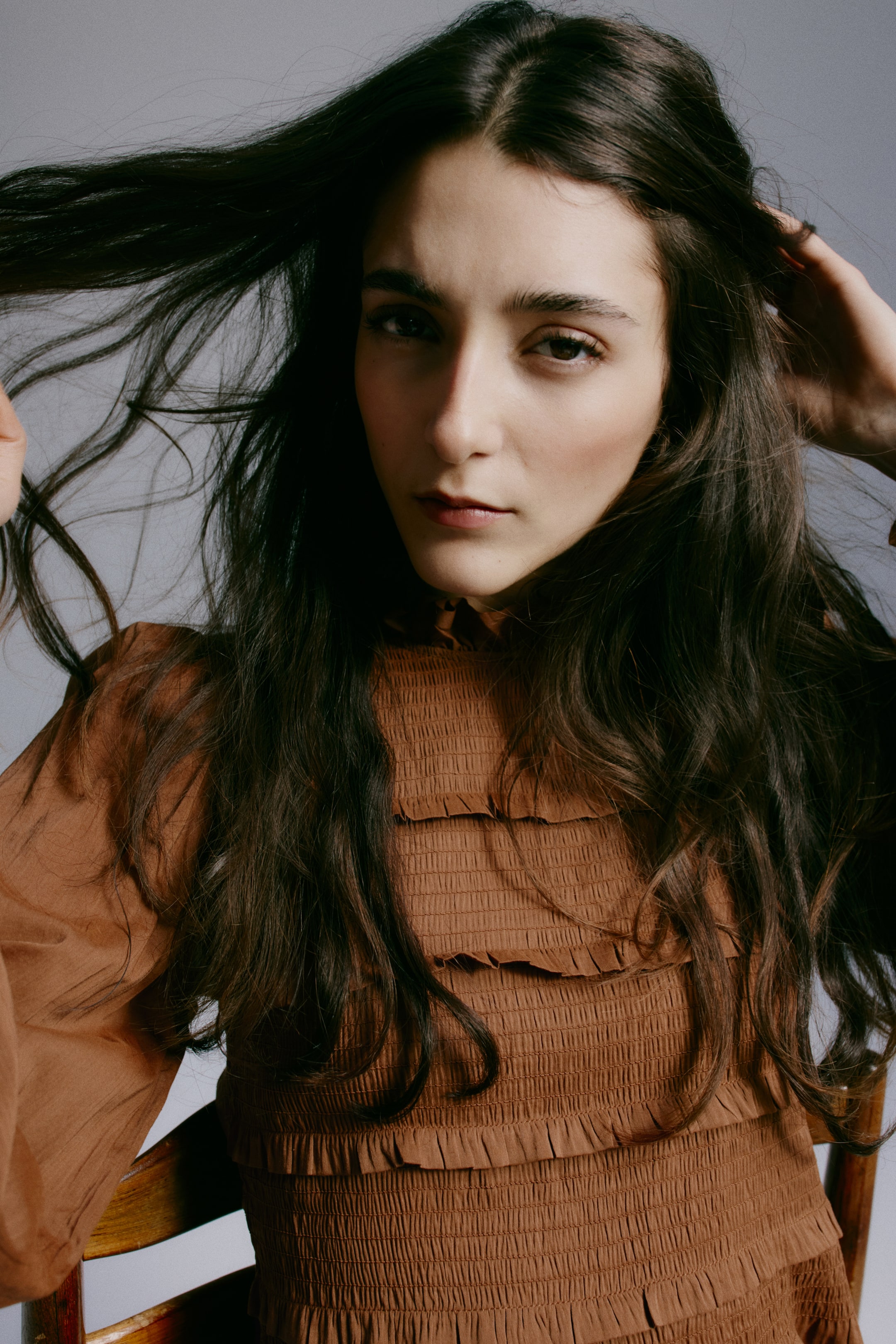 Ampliar la imagen: Una blusa marrón óxido presenta un cuello alto con volantes y mangas largas voluminosas. Su cuerpo exhibe un extenso fruncido con varios niveles de volantes horizontales.