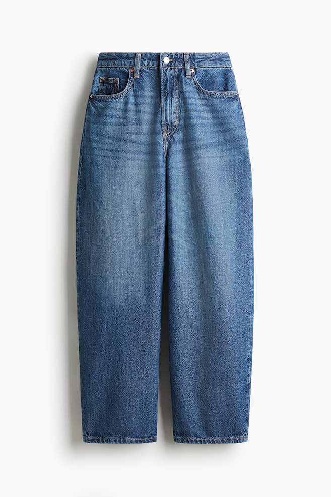 FRONT : Une paire de jeans en denim de coton à 5 poches est présentée, avec une taille haute, une fermeture éclair et un bouton. Le jean présente une jambe courbée et volumineuse qui est ample de la hanche à la cuisse, puis passe à une coupe ample et fuselée de la cuisse à l'ourlet. - 1