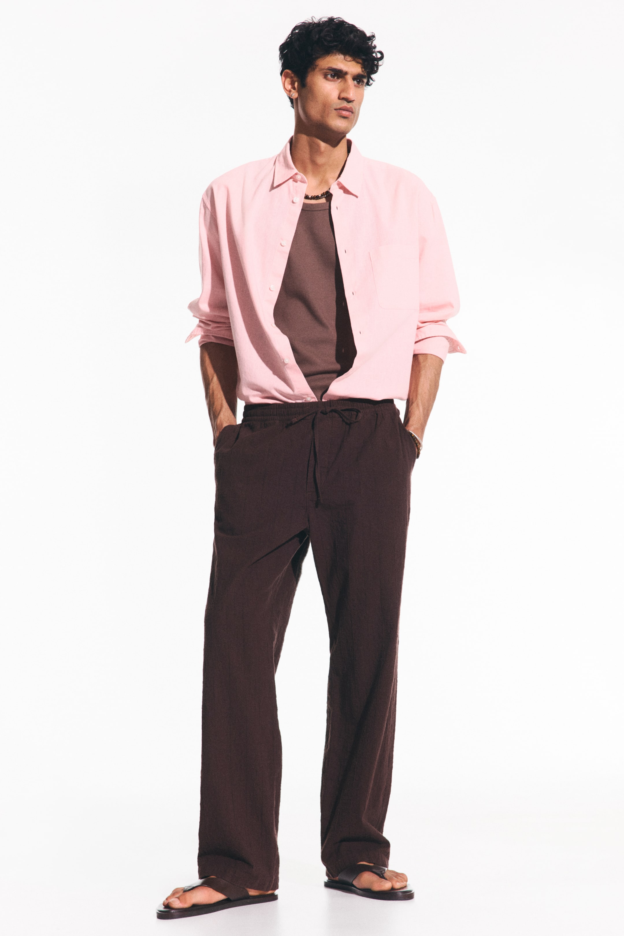 View larger image: Brown trousers showcase a laid-back, straight-leg design in a deep brown, textured material, complete with an elasticated waistband and a prominent drawstring tie at the front.