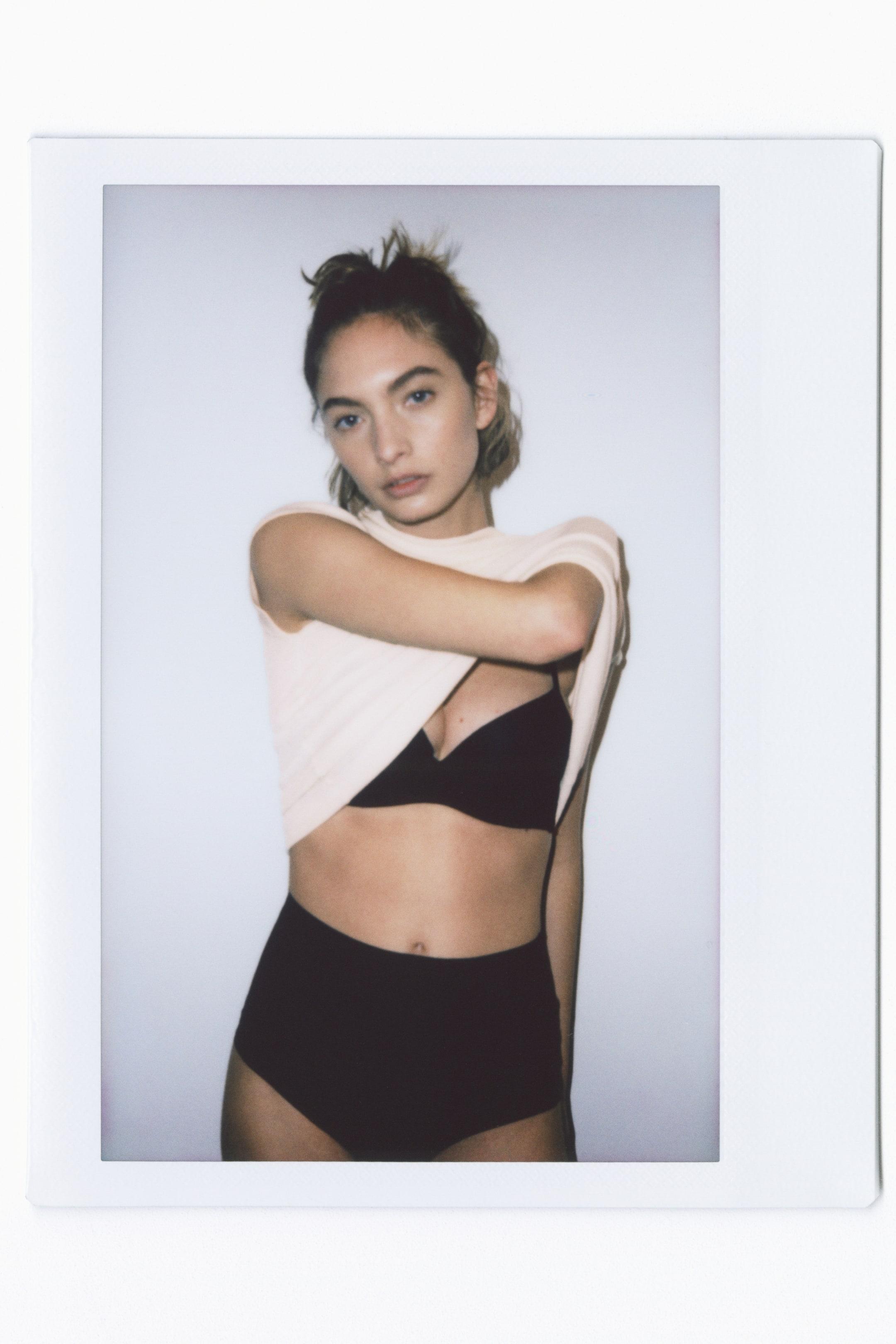 View larger image: "A black bra and black high-waisted briefs are showcased from a subtle front-right angle. A light pink top is lifted, unveiling the bra's minimalist cups and the high-waisted style of the briefs."