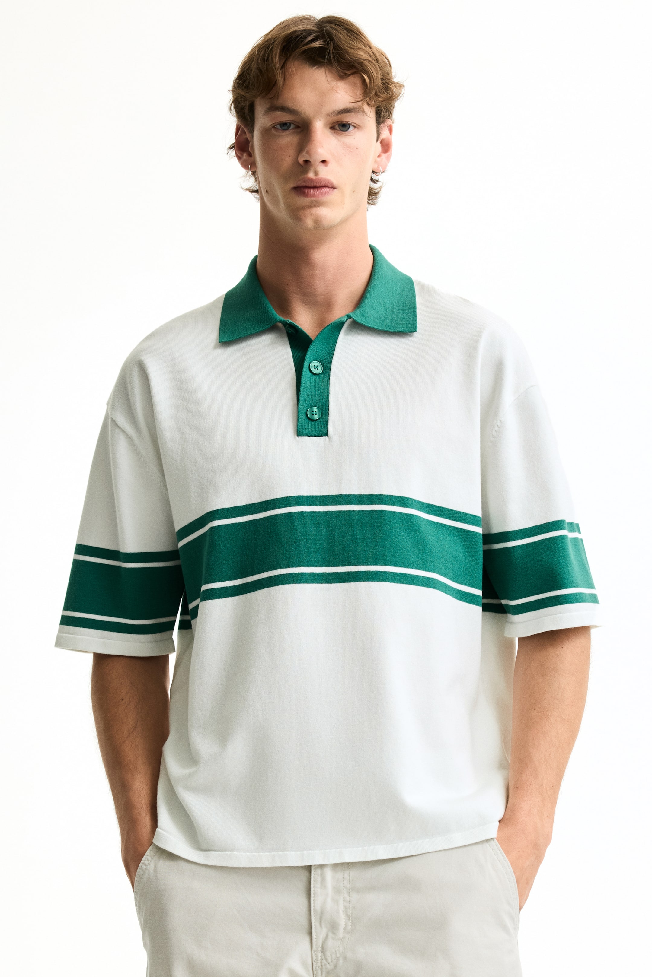 View larger image: A white knit polo shirt is facing forward, featuring a ribbed green collar and a green two-button placket. Two horizontal green stripes, each framed by thin white lines, extend across the chest and short sleeves.