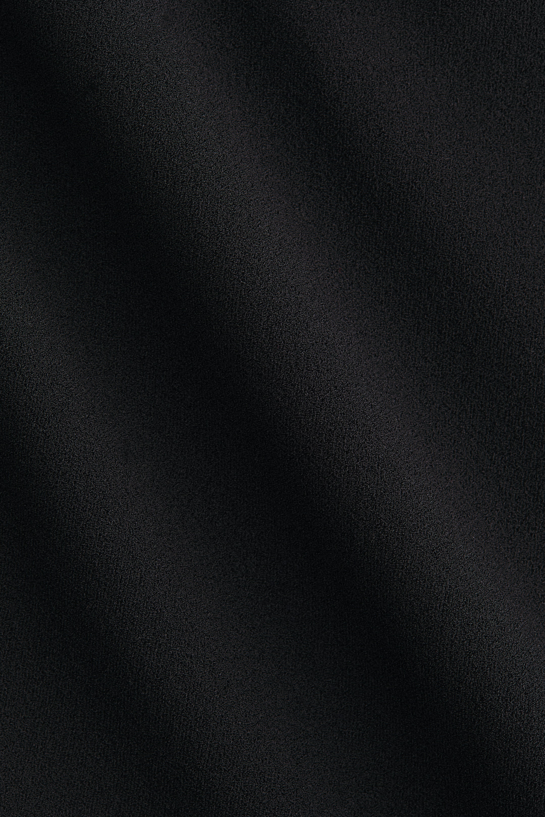 Xem ảnh lớn hơn: Chiếc váy quần jersey hiển thị bề mặt màu đen với kết cấu tinh tế, kèm theo các nếp gấp nhẹ và biến đổi ánh sáng tinh tế.