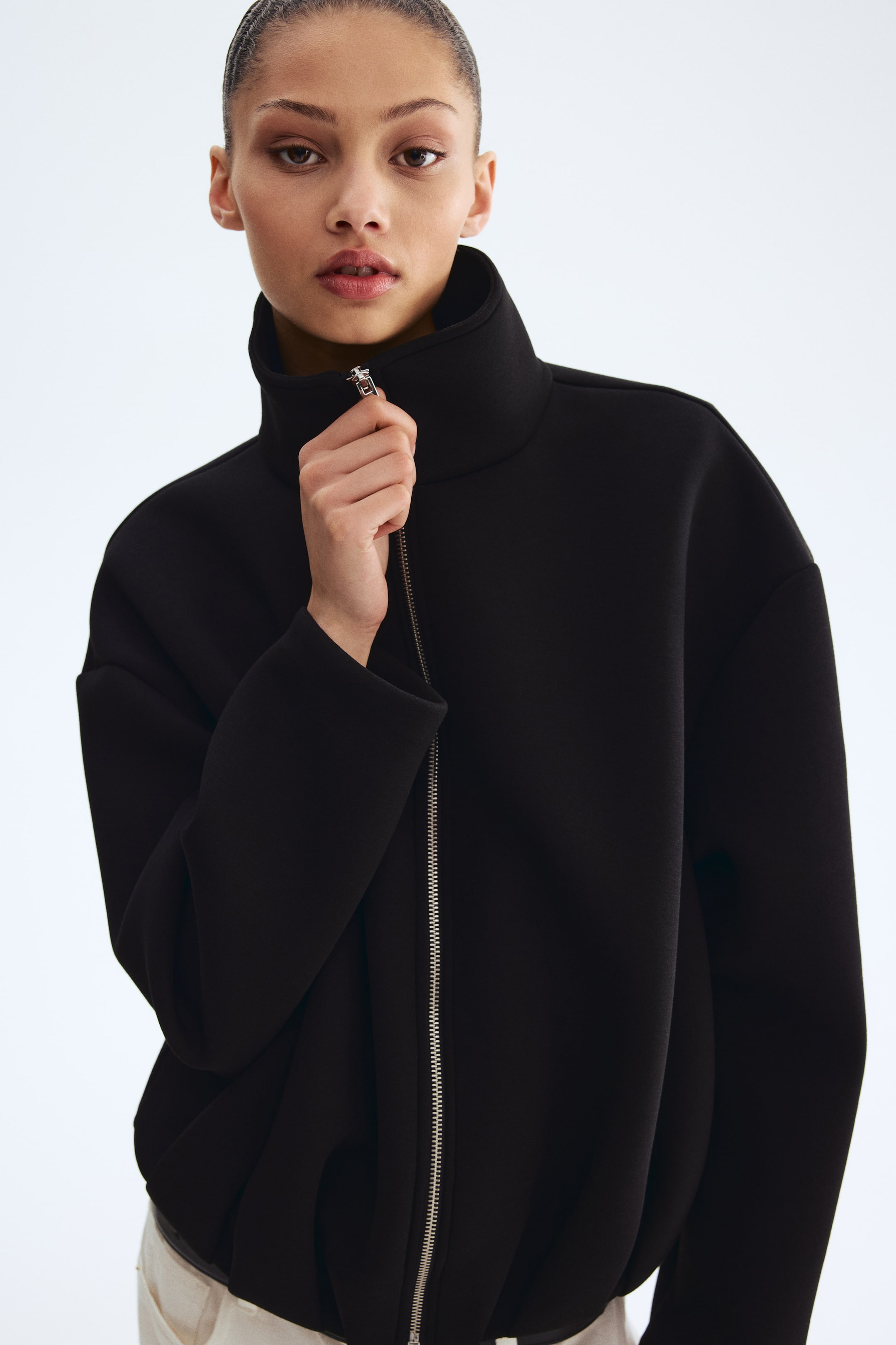 View larger image: A black high-neck jacket is showcased front-facing, featuring a standing collar, a silver-toned front zipper, and voluminous dropped-shoulder sleeves.