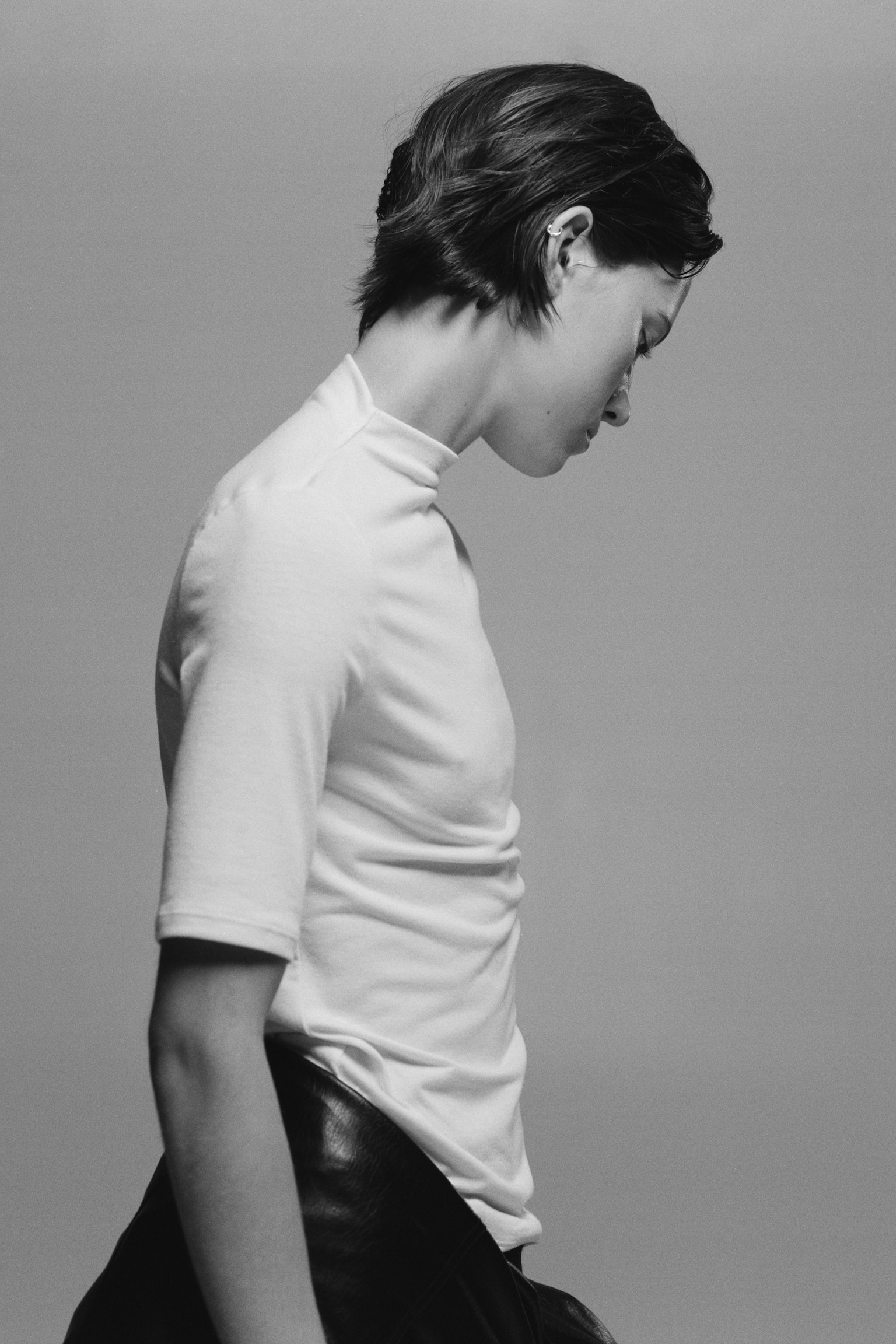 A solid white mock neck T-shirt is shown from the back, featuring elbow-length short sleeves and a straight hem. The garment showcases a clean, smooth knit texture with a slightly raised neckline. - 1